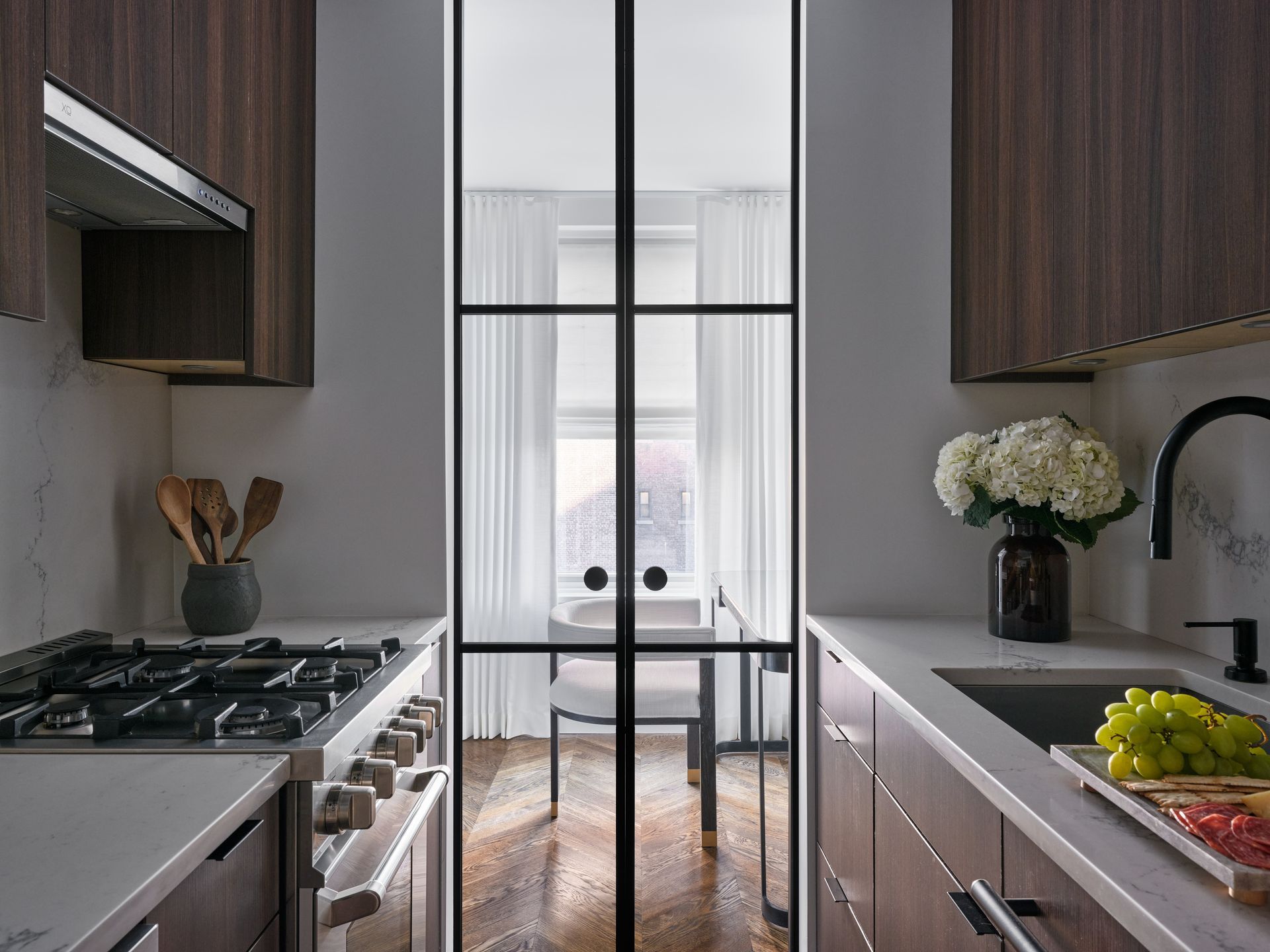 Modern kitchen with dark cabinets, white countertops, and a narrow windowed dining nook.