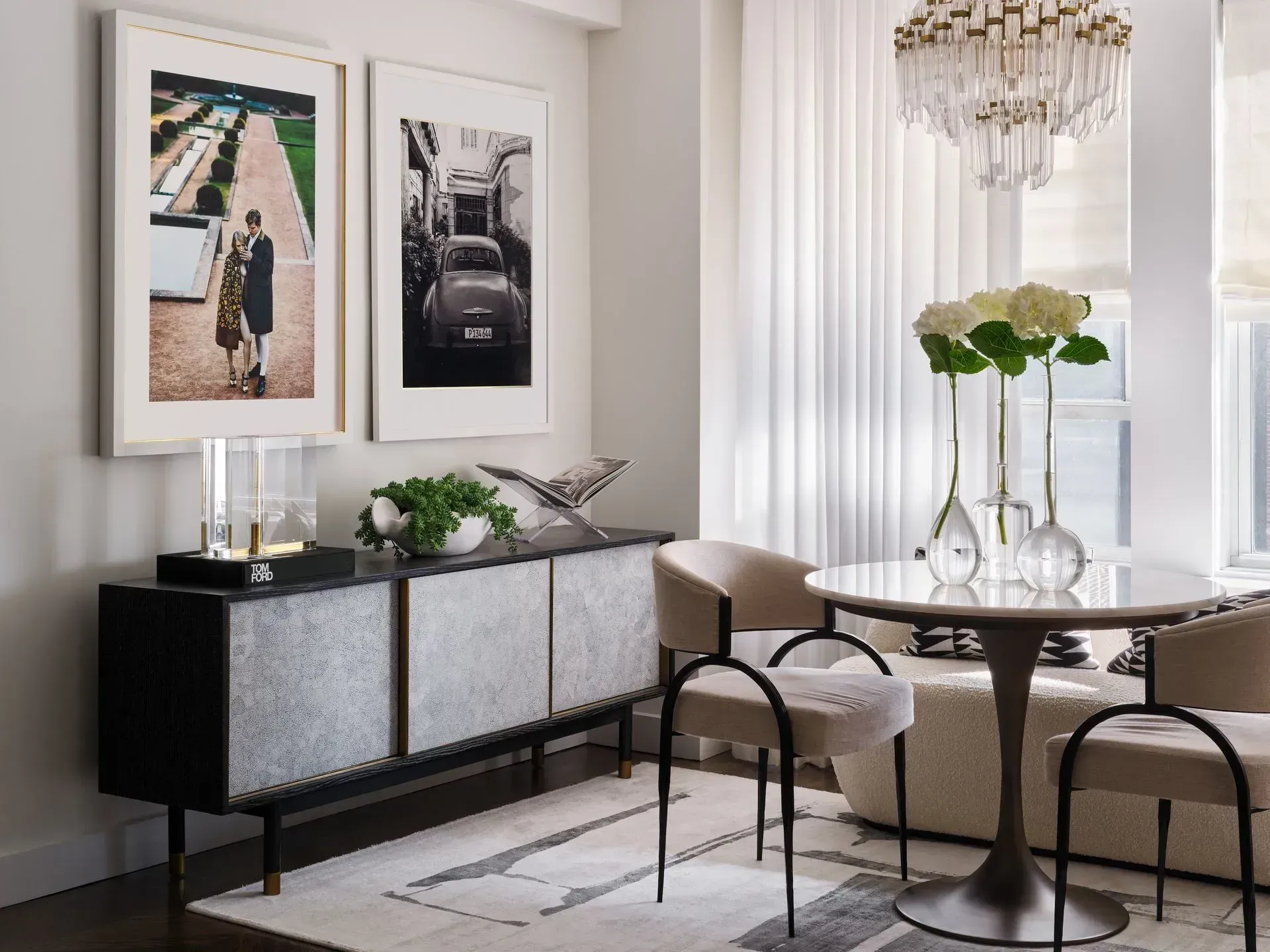 Elegant dining room with round glass table, upholstered chairs, black sideboard, and framed art.