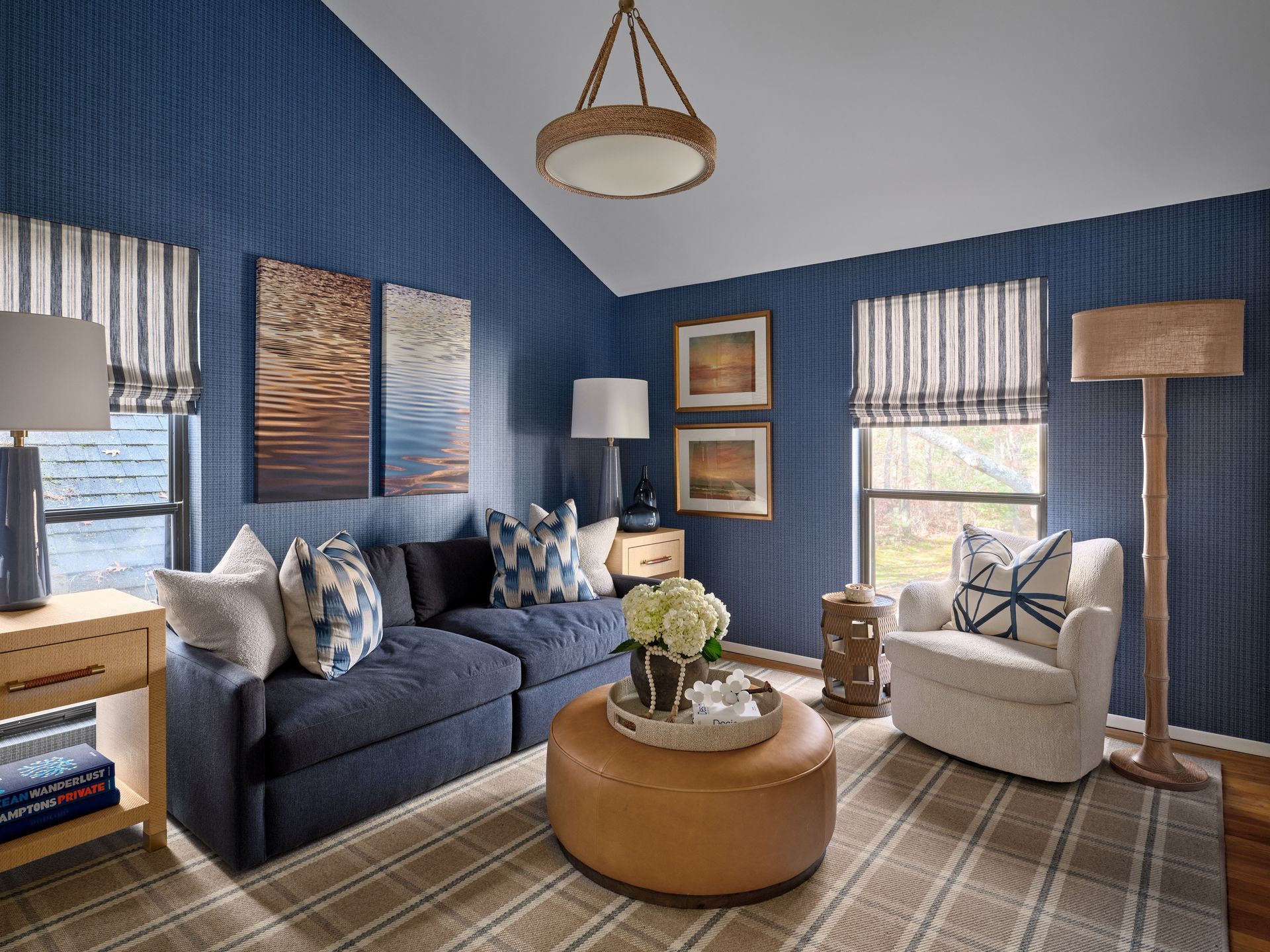 Blue living room with navy sofa, cream chair, round ottoman, and striped curtains on blue walls.