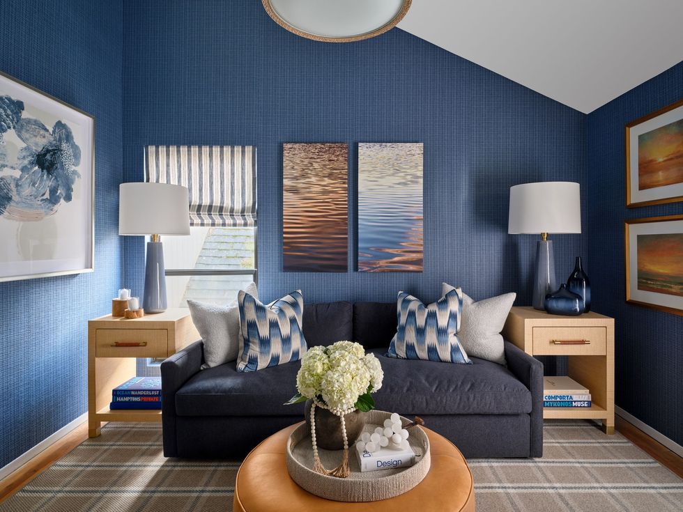 Blue living room with gray sofa, patterned pillows, lamps, wood tables, and wall art under vaulted ceiling