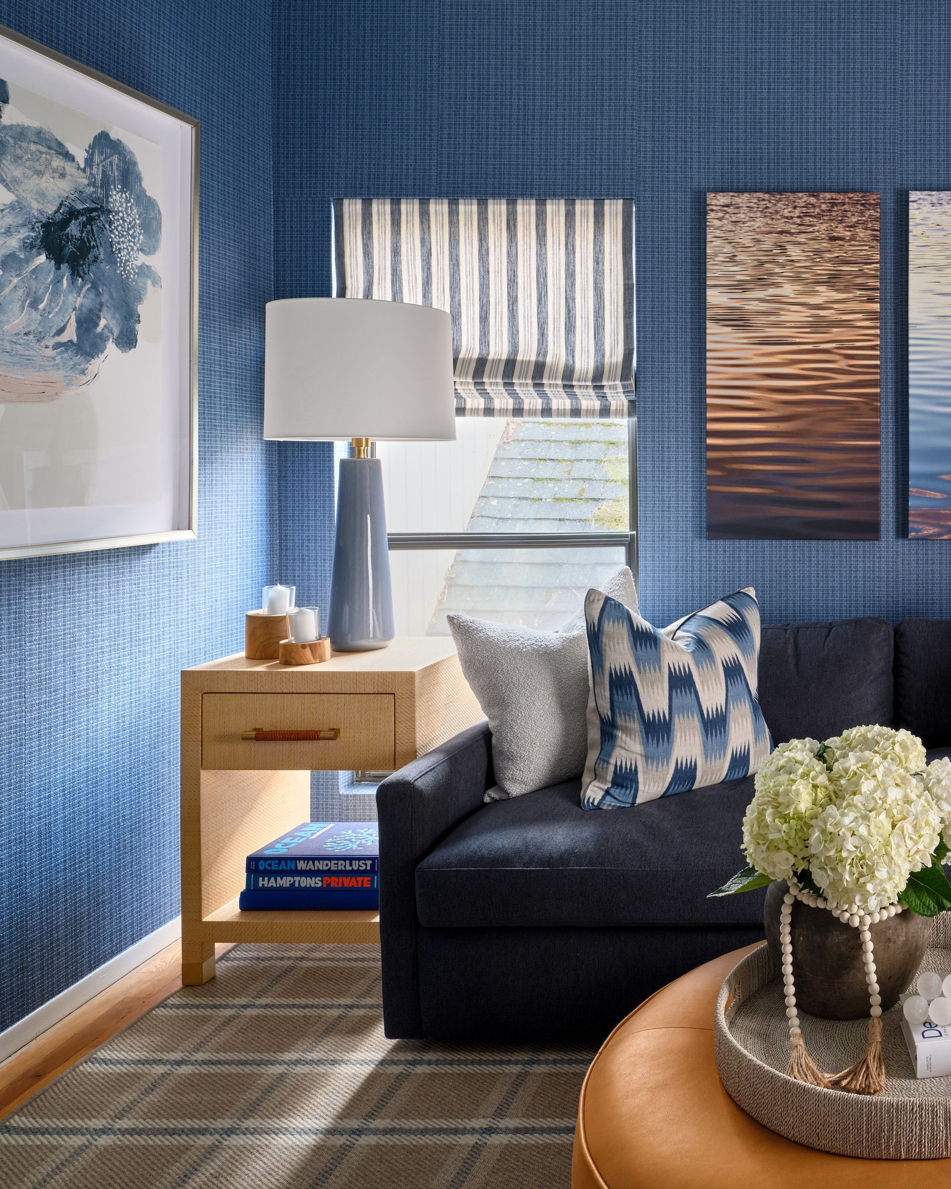Blue-walled living room with a dark sofa, patterned pillows, lamp, side table, and floral centerpiece