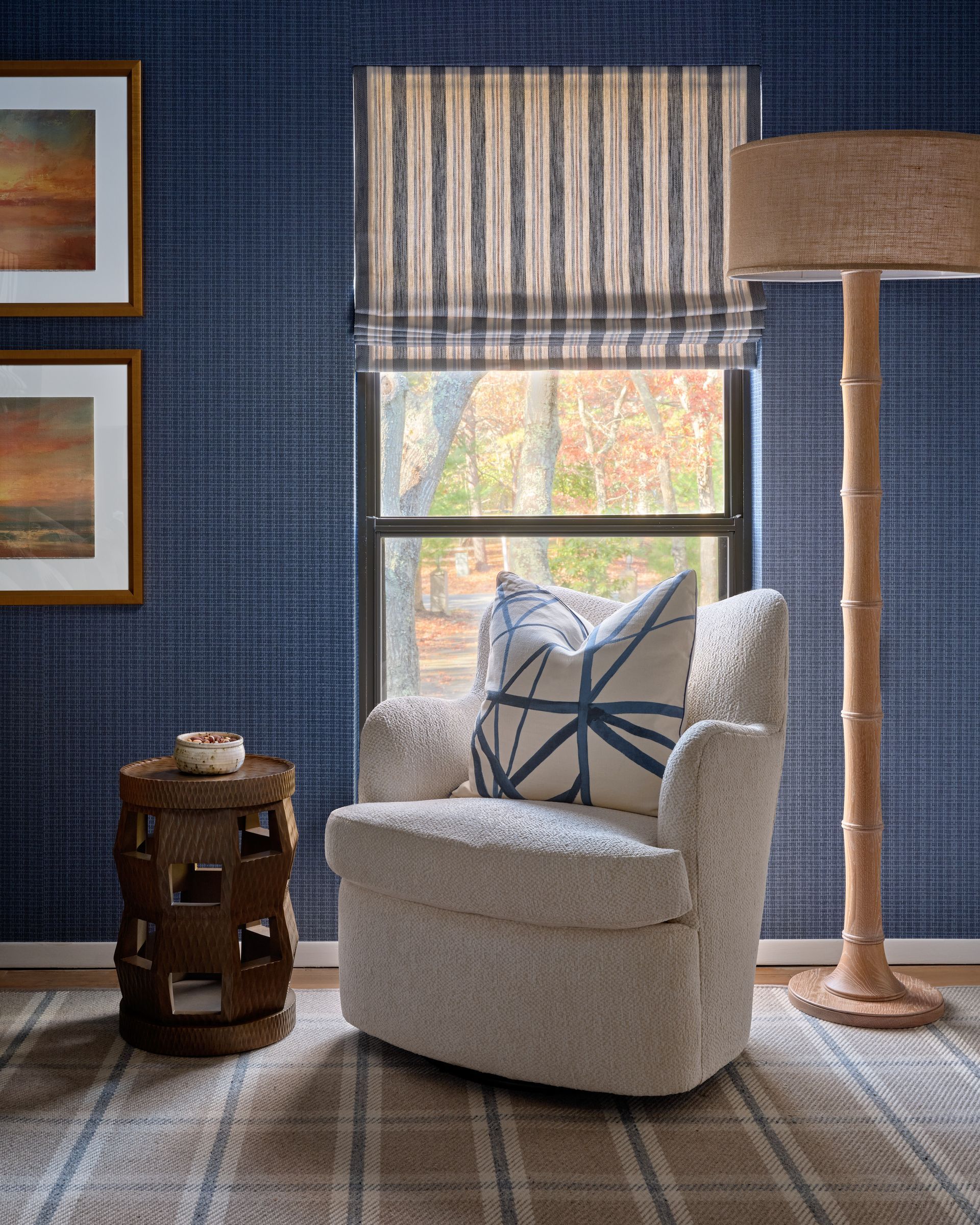 Cozy blue bedroom with white swivel chair, striped pillow, floor lamp, and window with striped shade
