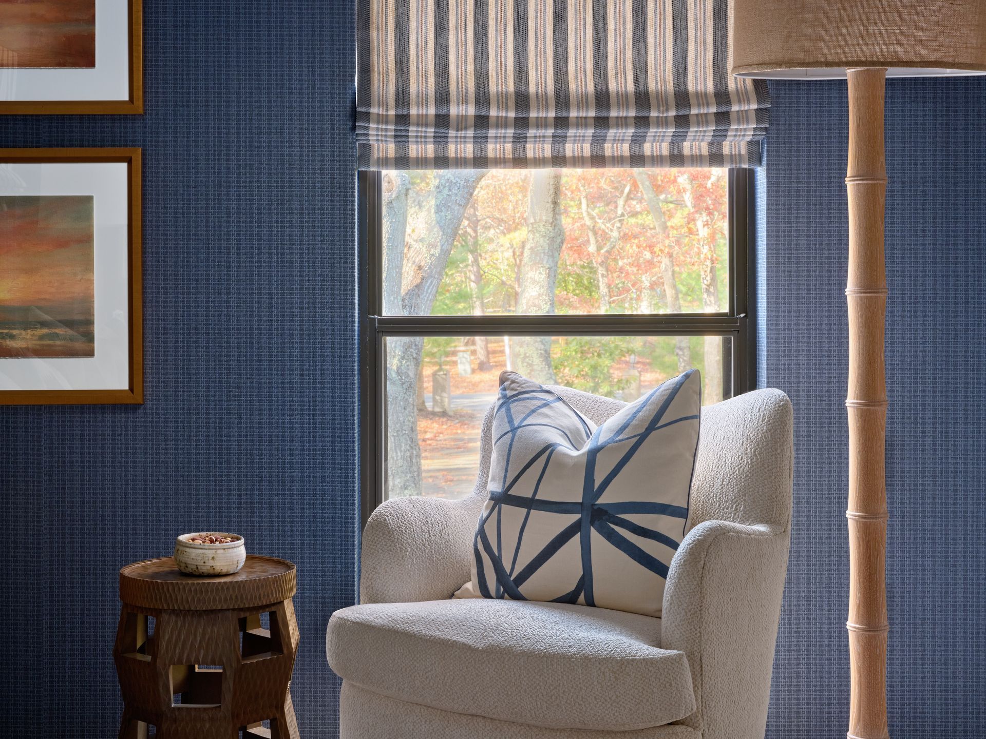 Cozy living room corner with a cream chair, patterned pillow, window, and blue textured wall.
