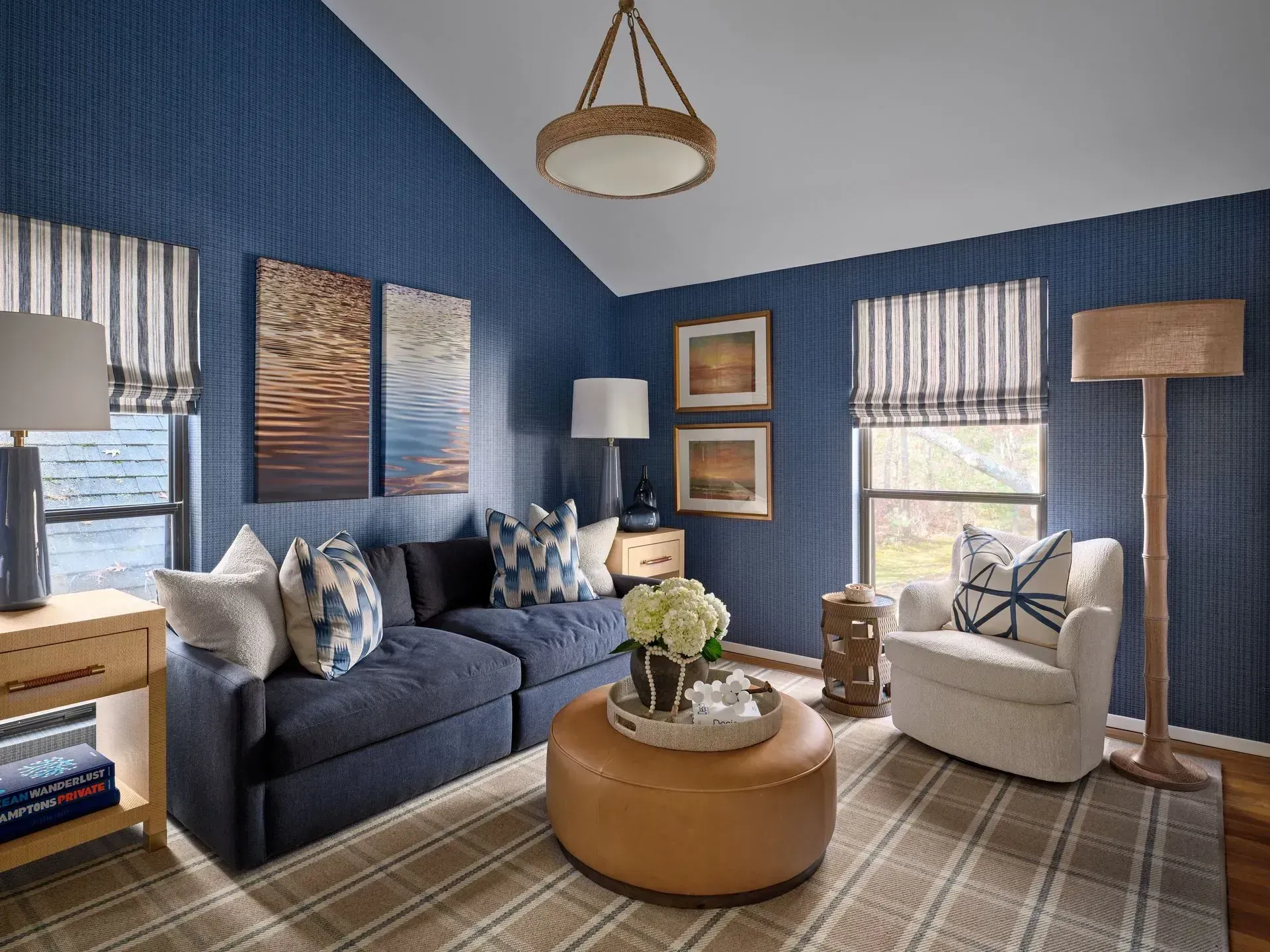 Blue living room with navy sofa, cream chair, round ottoman, and striped curtains on blue walls.