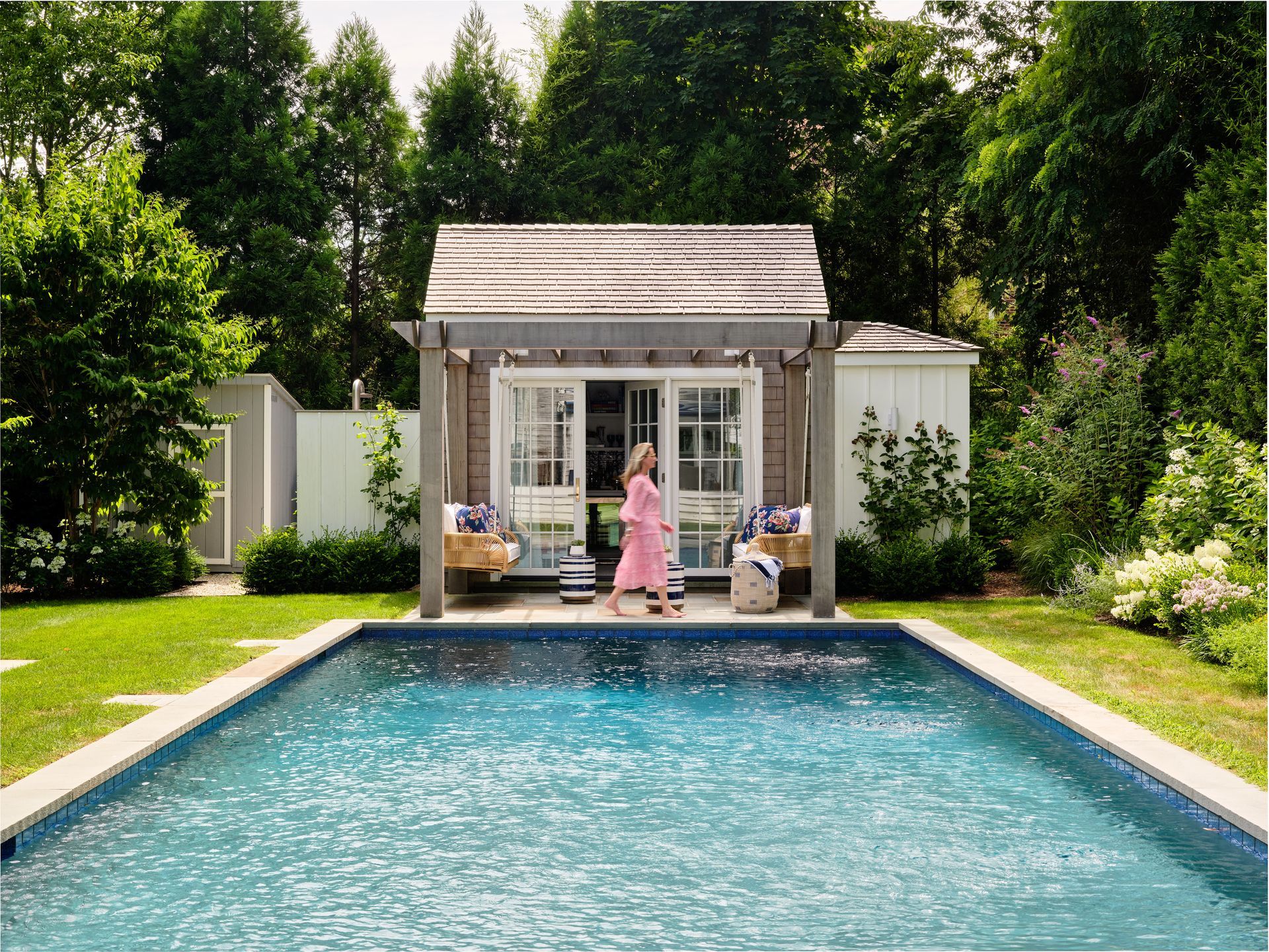 Backyard pool with a small cottage, patio furniture, and a person in pink standing at the doorway