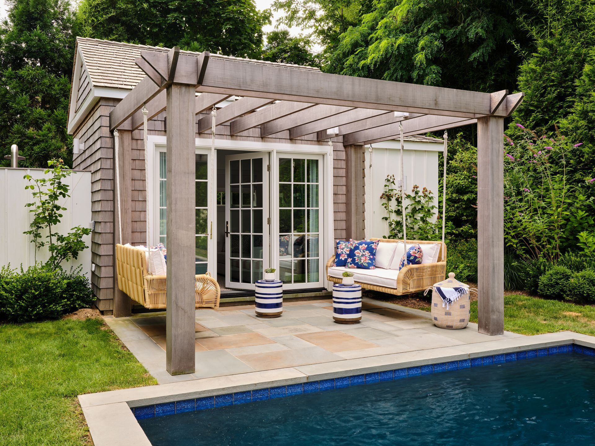 Pergola-covered patio with wicker seating beside a backyard swimming pool