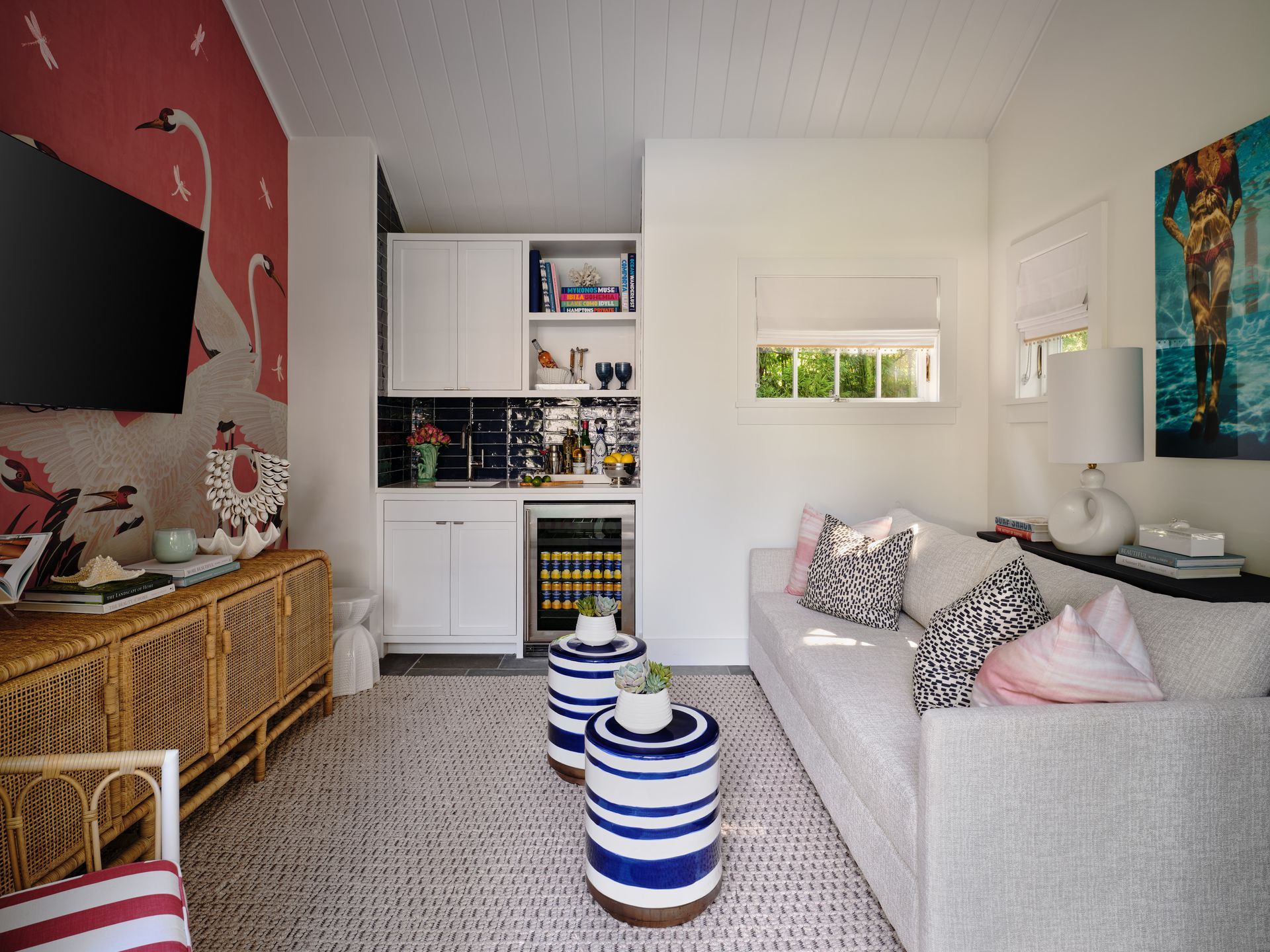 Bright living room with gray sofa, wicker TV stand, striped poufs, and built-in shelves in a white alcove