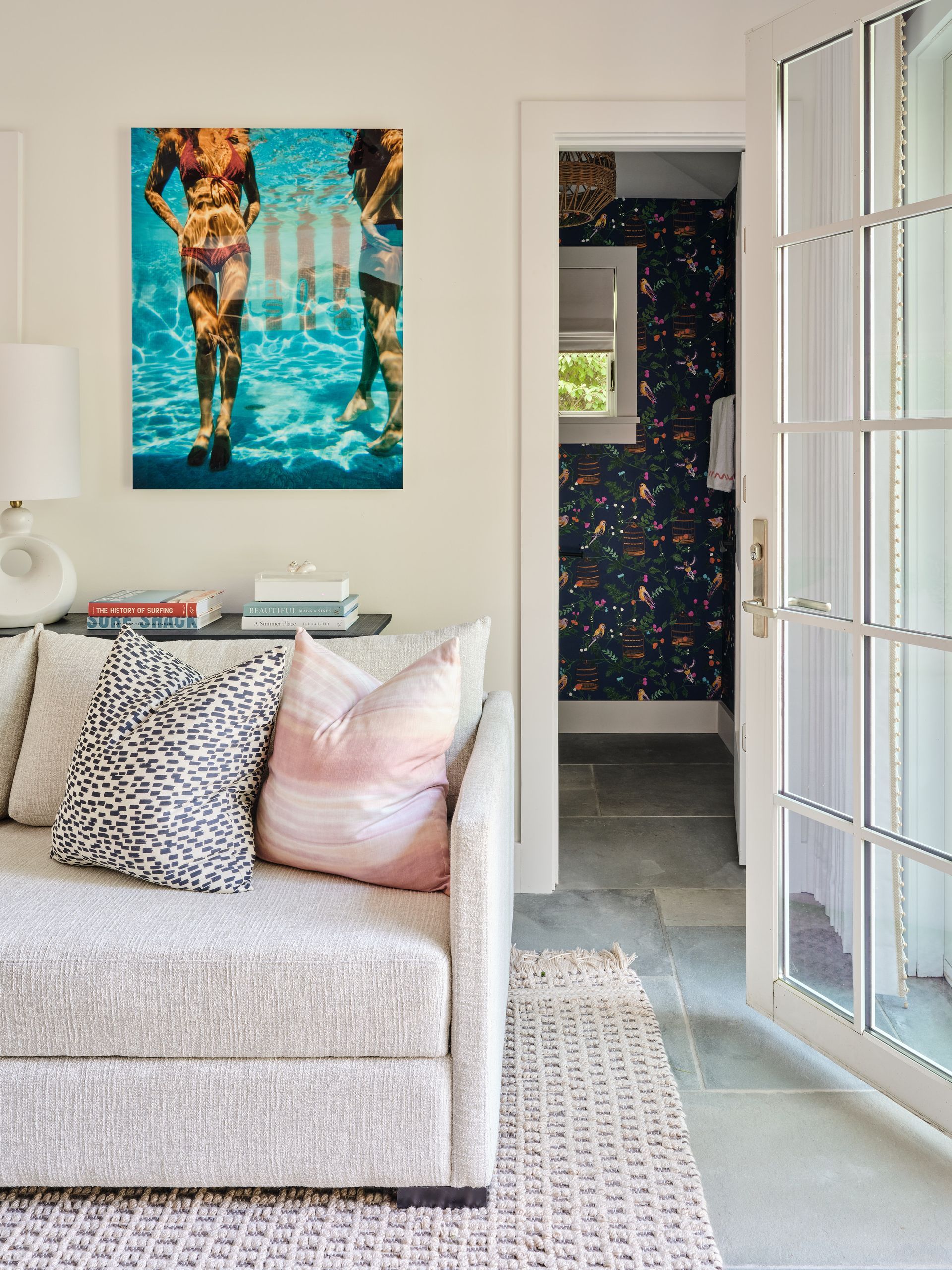 Bright living room with a cream sofa, pink and leopard pillows, and a colorful wall painting by an open doorway.