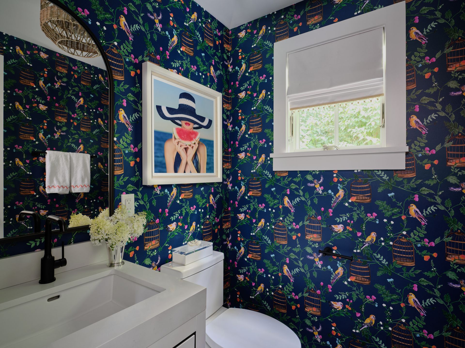 Modern bathroom with navy floral wallpaper, white vanity, and a framed art print by a window