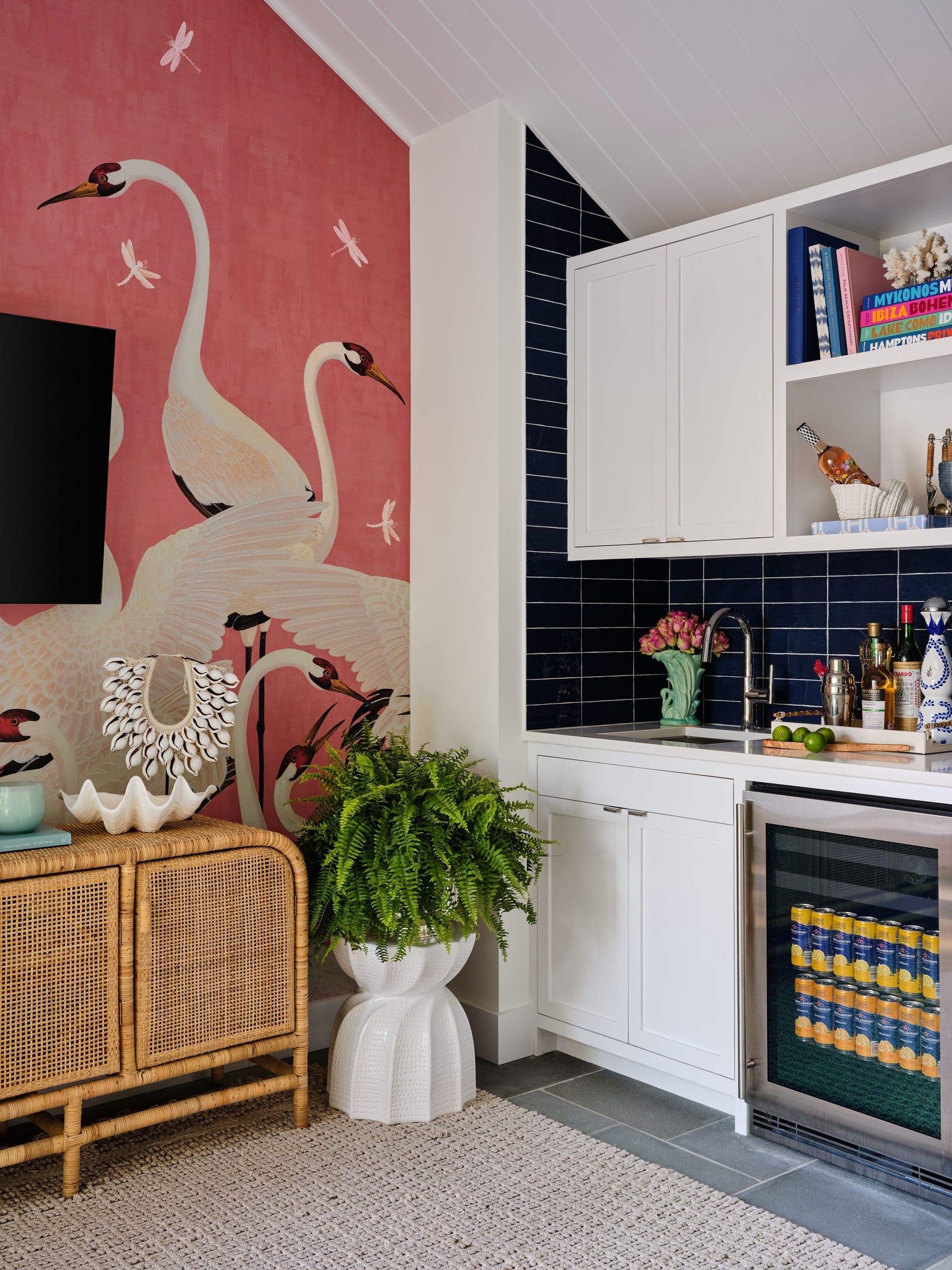 Stylish kitchen corner with pink flamingo wall mural, white cabinets, wicker console, and plants