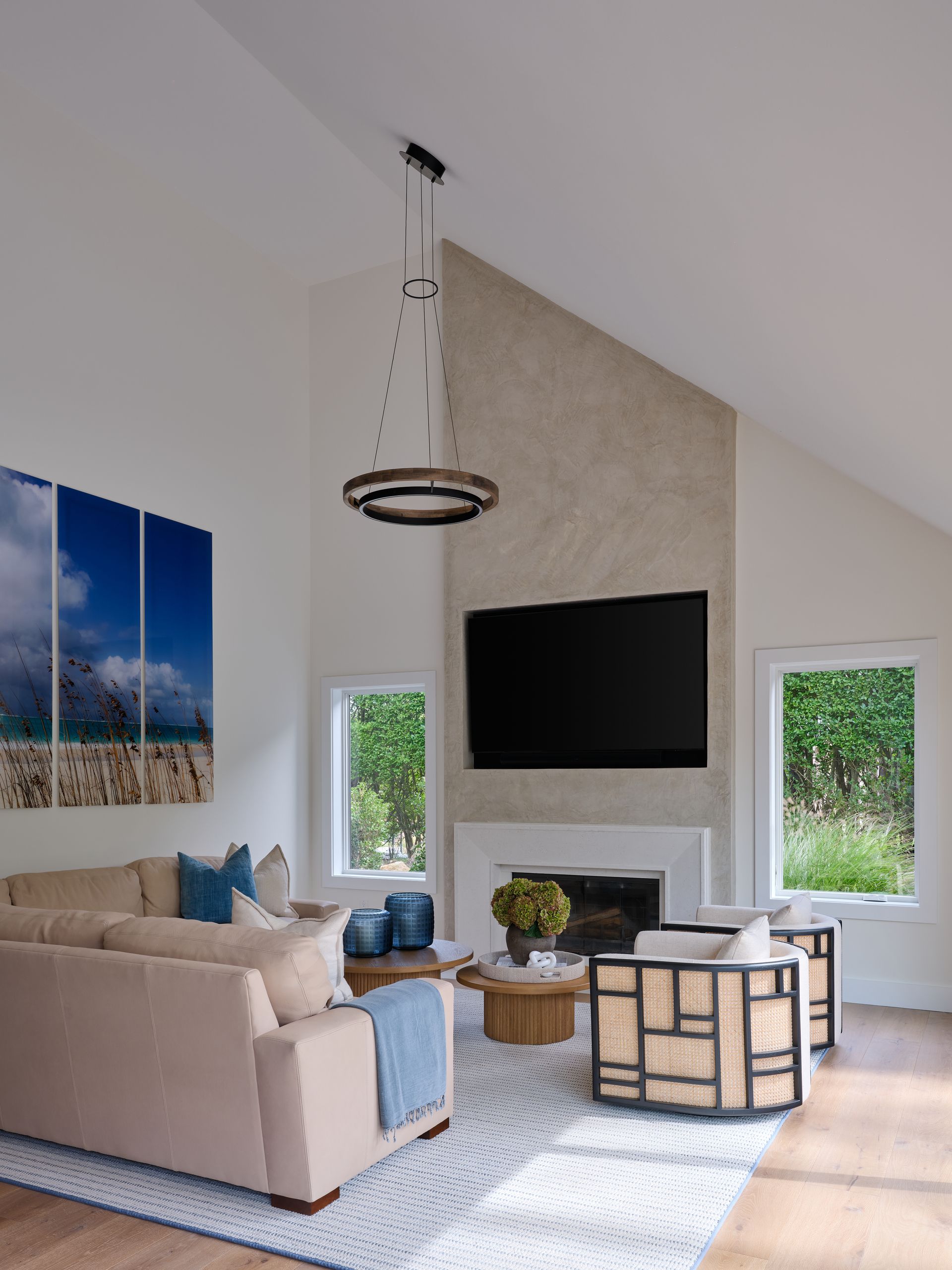 Bright living room with beige sectional, wall-mounted TV above fireplace, and blue landscape art.