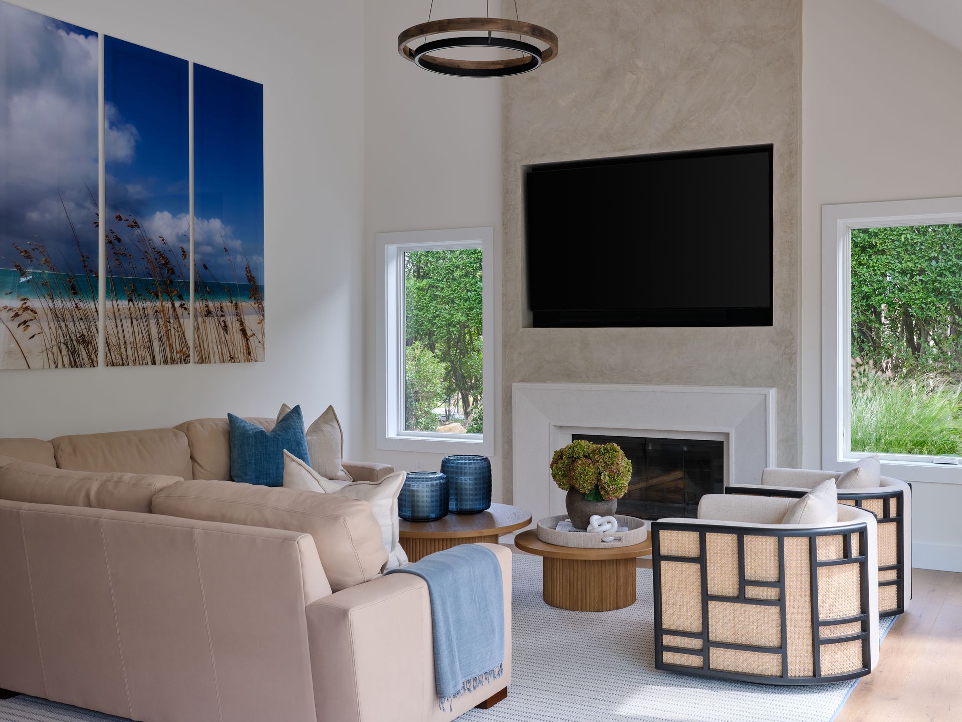 Bright living room with beige sofa, wall-mounted TV, fireplace, and coastal artwork
