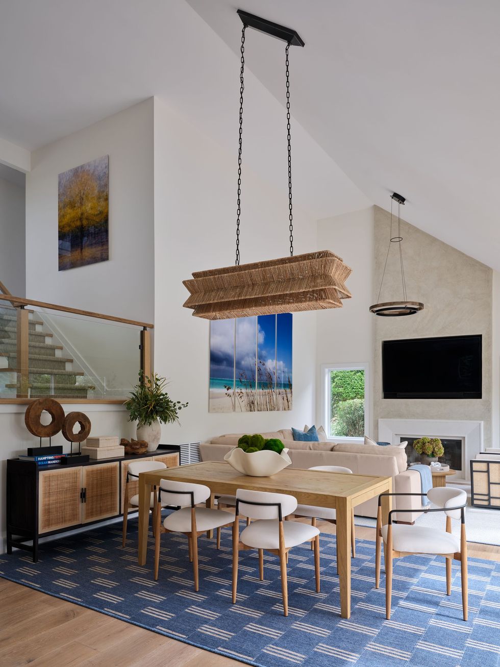 Modern dining room with woven pendant light, blue rug, wood table, and fireplace TV area