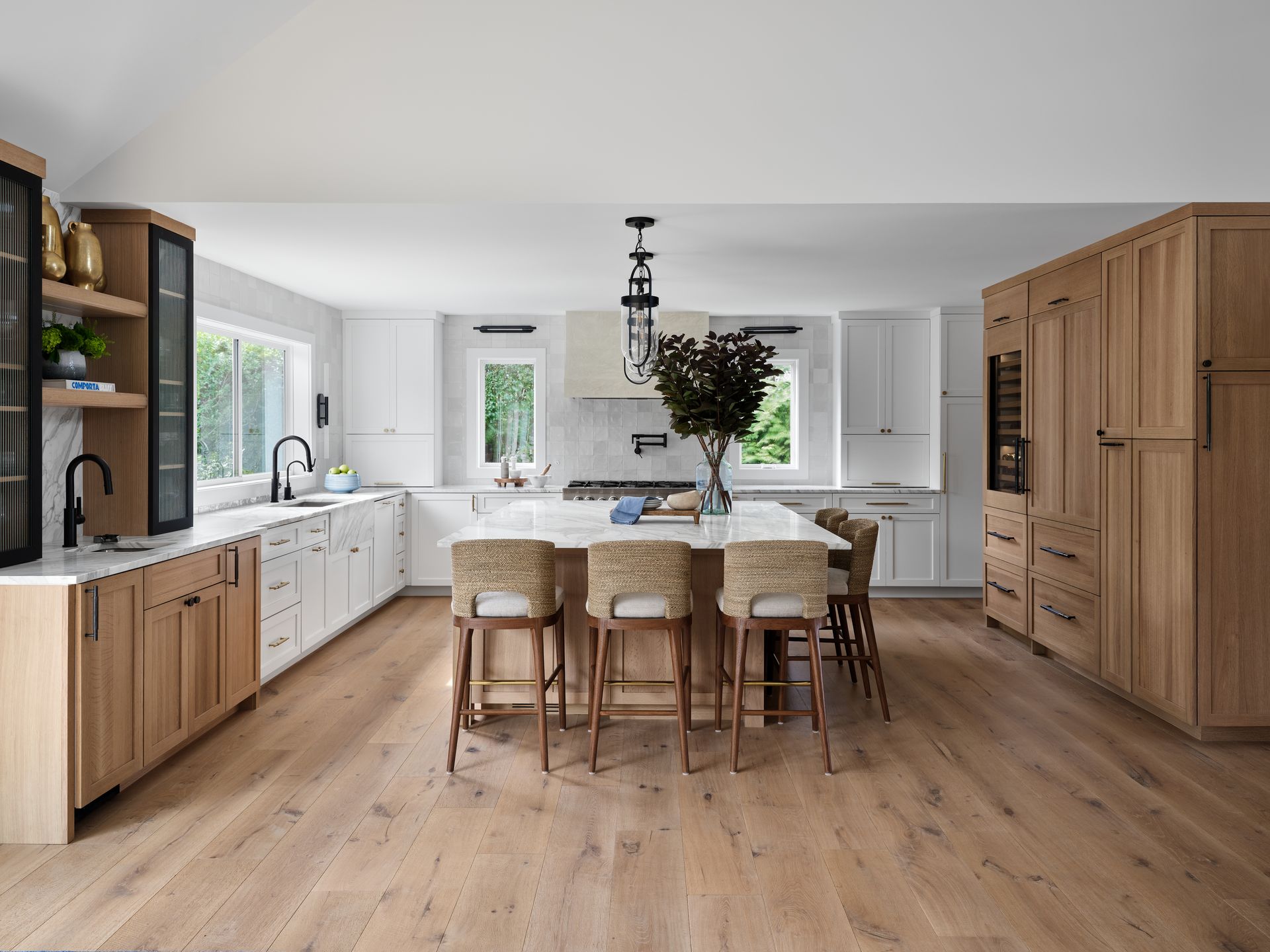 Bright modern kitchen with wood cabinets, white countertops, and a dining island with woven chairs.