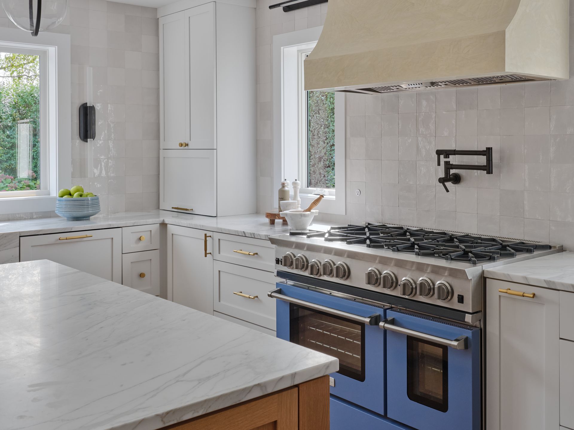 Bright white kitchen with marble island, white cabinetry, and stainless steel stove beneath a beige hood