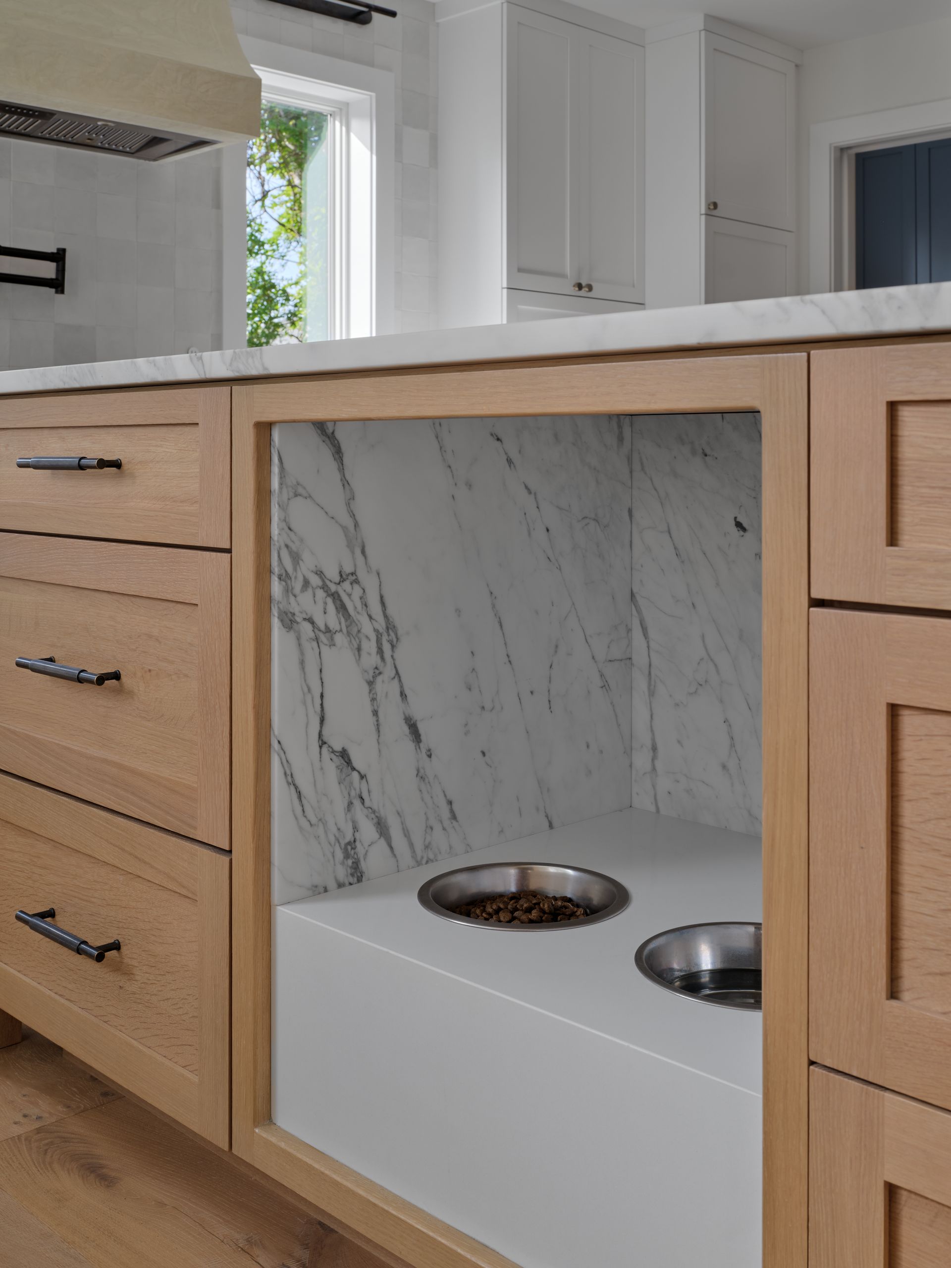 Kitchen island with wood cabinets, marble shelf, and built-in pet feeding bowls underneath