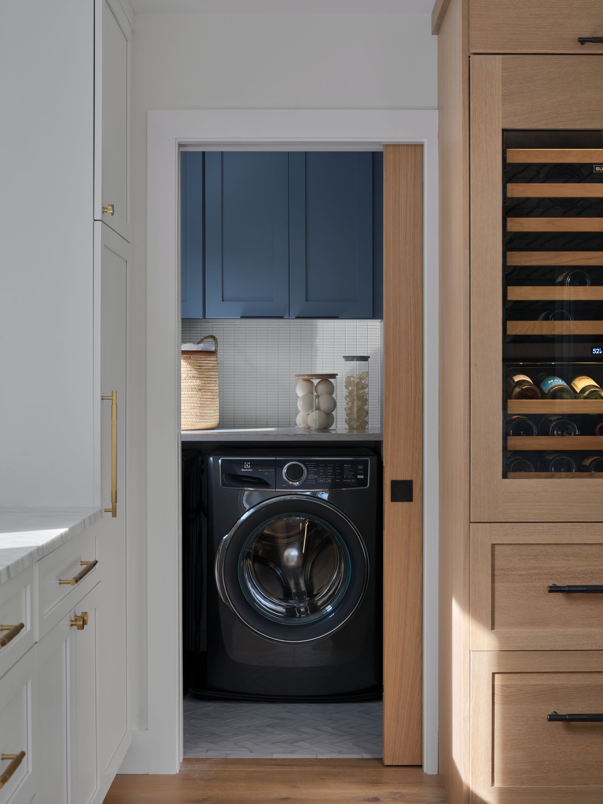 Laundry room doorway with a black front-loading washer under blue cabinets and wood shelving nearby