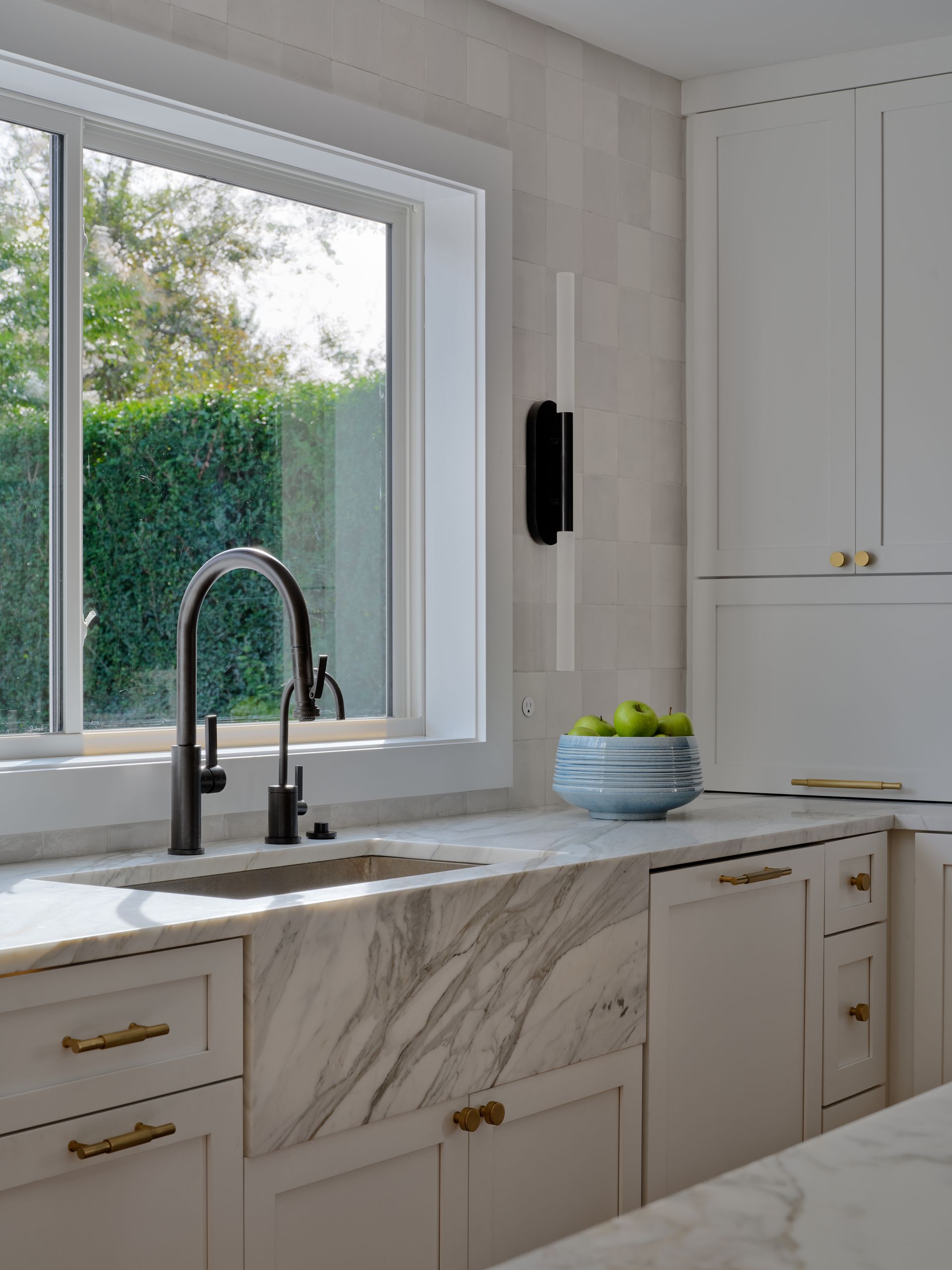Bright modern kitchen with marble countertop, black faucet, and window view of greenery