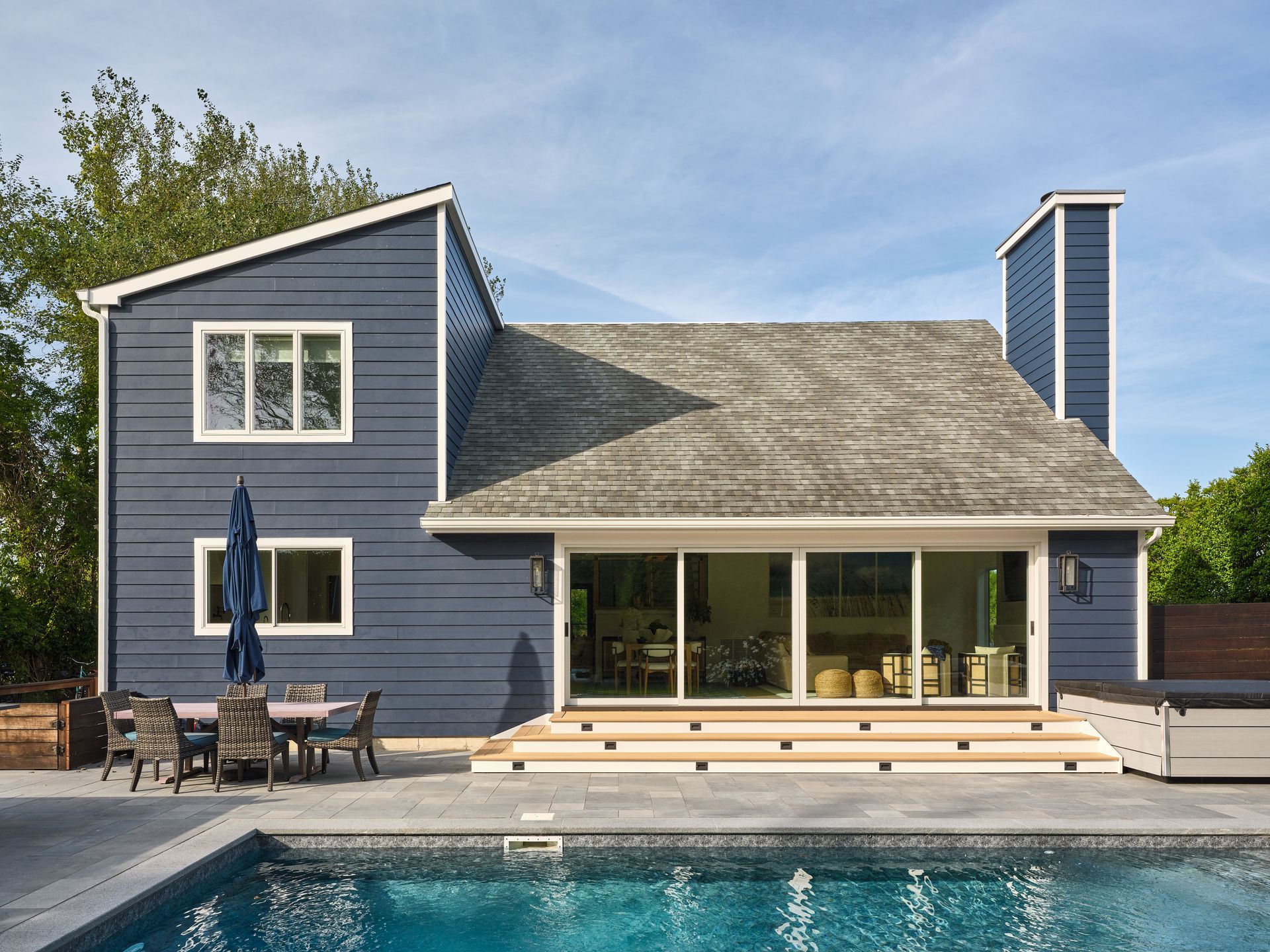 Blue-gray lakeside house with large windows, deck, and patio furniture beside the water