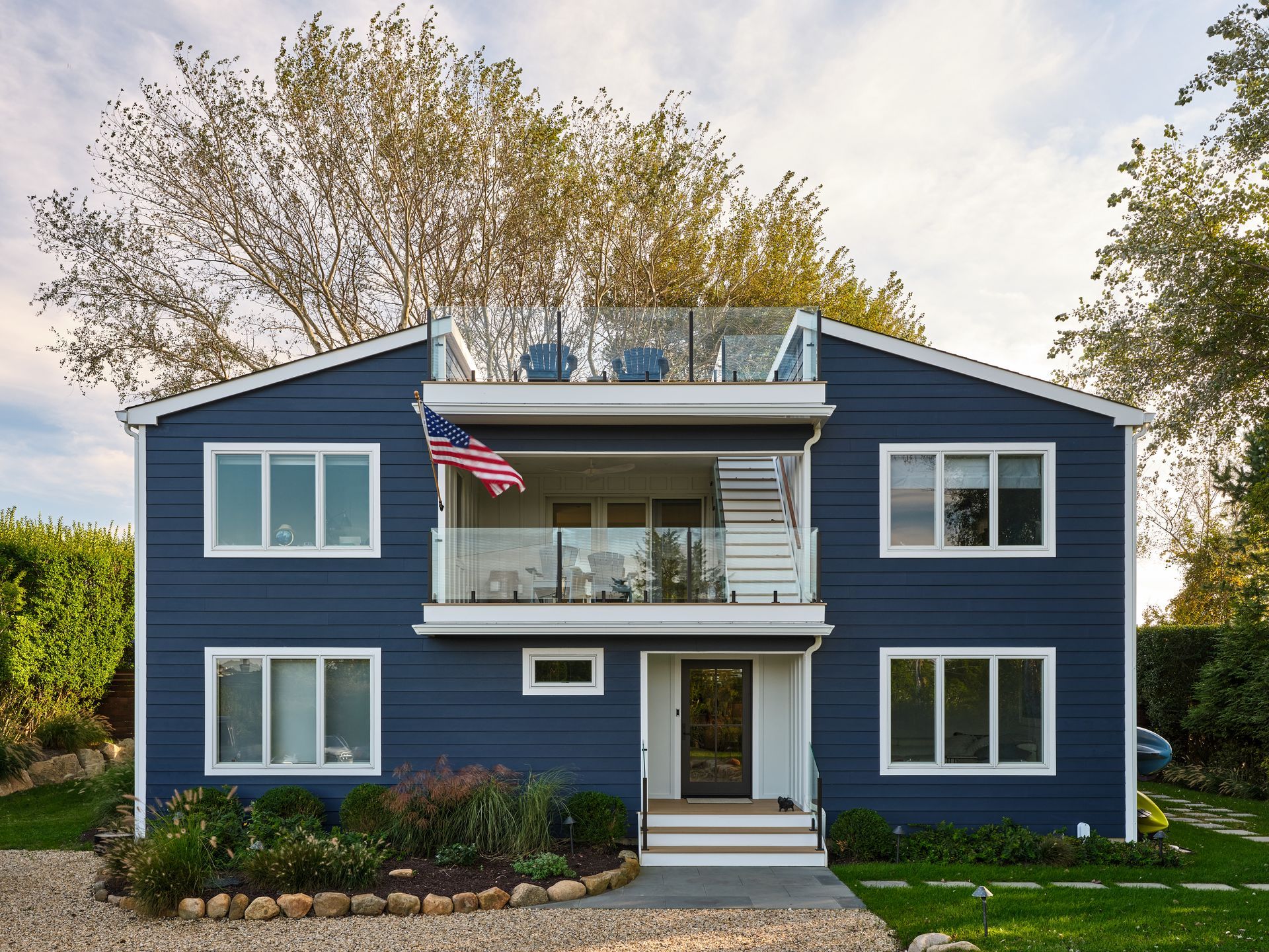 Blue two-story house with white trim, balcony, and an American flag in front