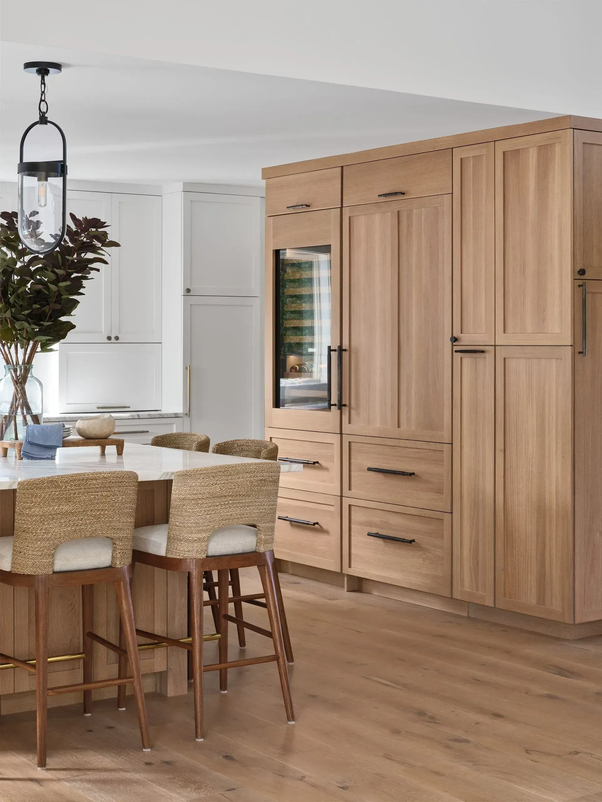 Modern kitchen with light wood cabinets, large island, bar stools, and pendant lighting