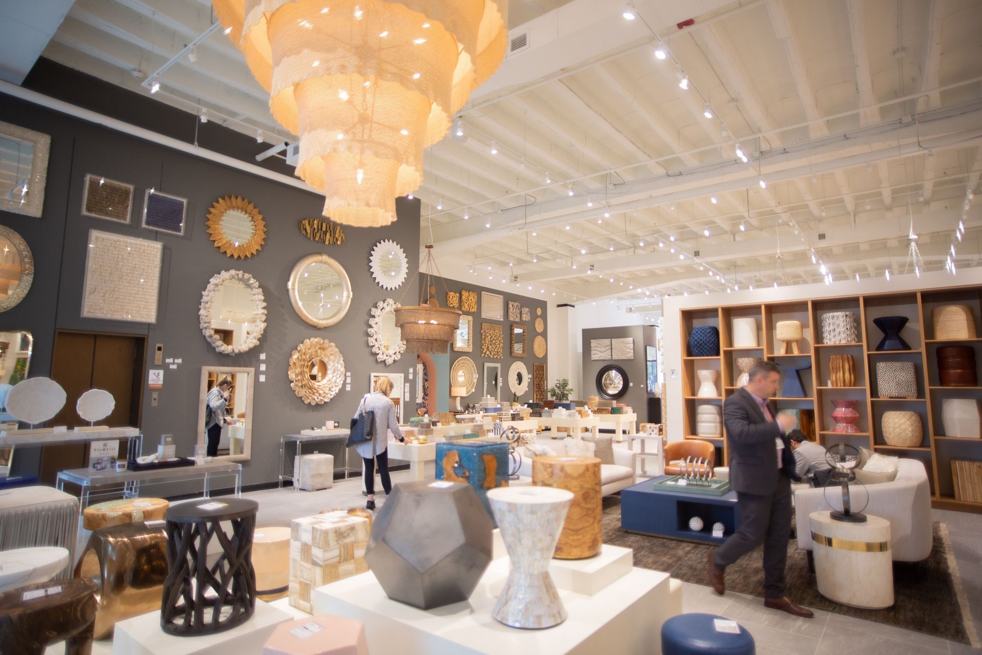 Upscale showroom with chandeliers, clocks, and modern furniture displays; two people browsing inside.