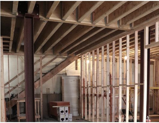 Unfinished basement with exposed wood framing, support beams, and stairs under construction