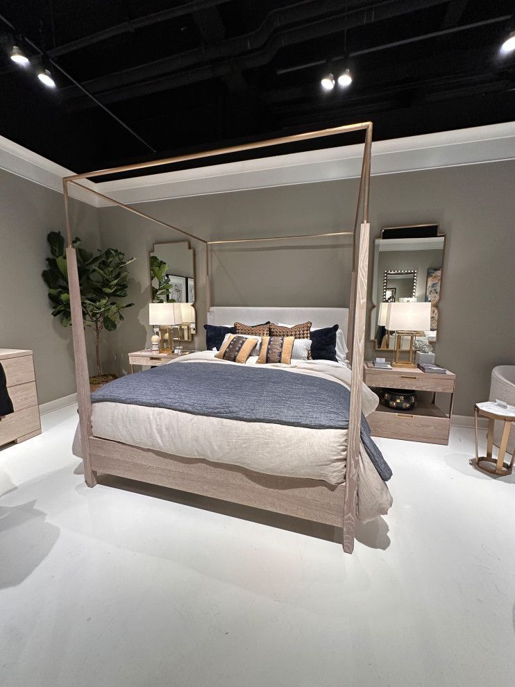 Modern bedroom display with a four-poster bed, blue bedding, lamps, mirrors, and neutral decor