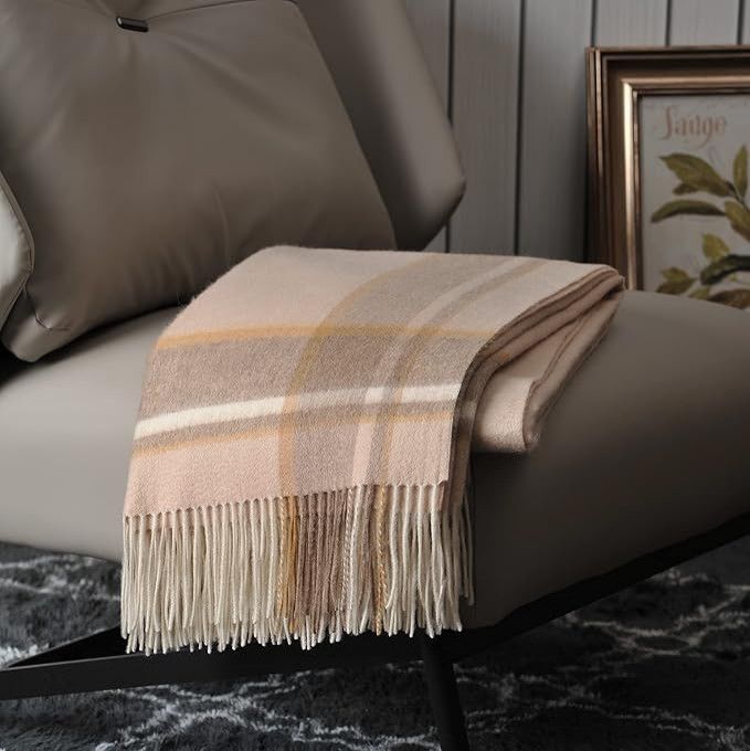 Folded beige plaid throw with fringe draped over a taupe chair in a cozy living room corner