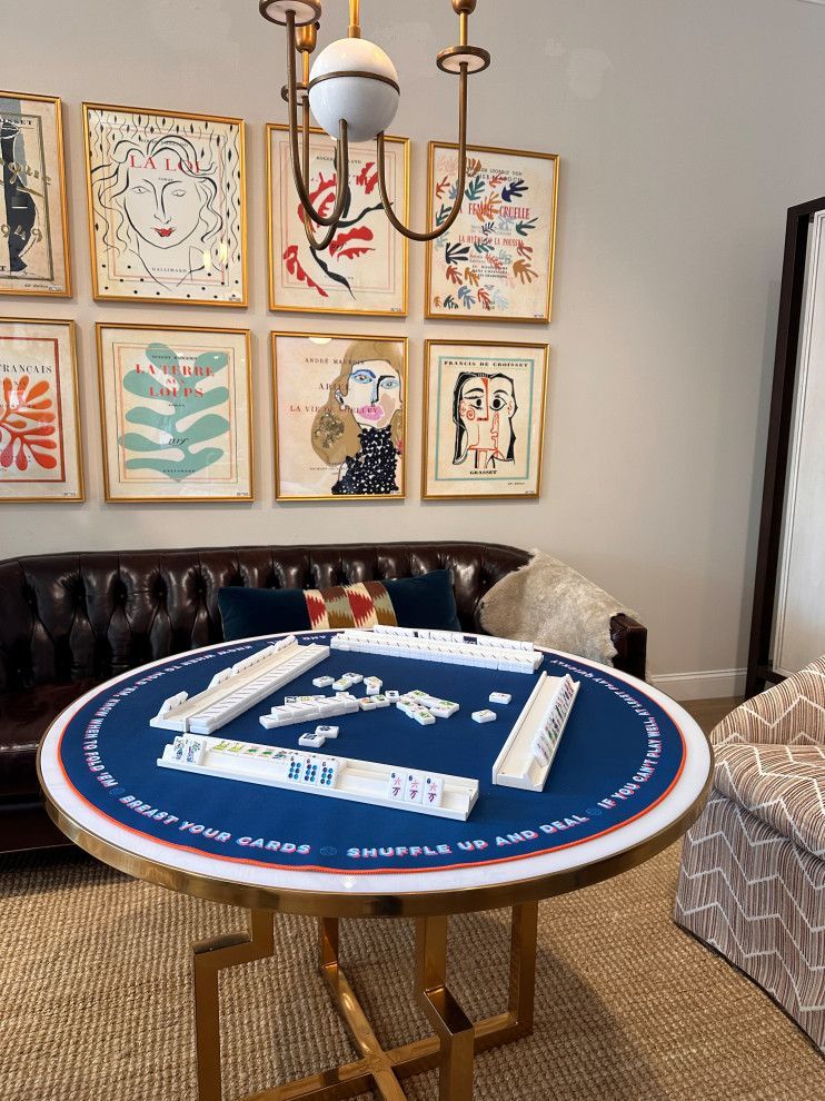 Round blue card table in a stylish living room with framed art and a chandelier.