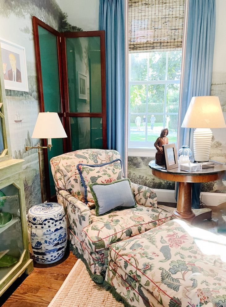 Cozy floral armchair and chaise in a bright room with blue curtains, lamps, and a round wooden table by the window