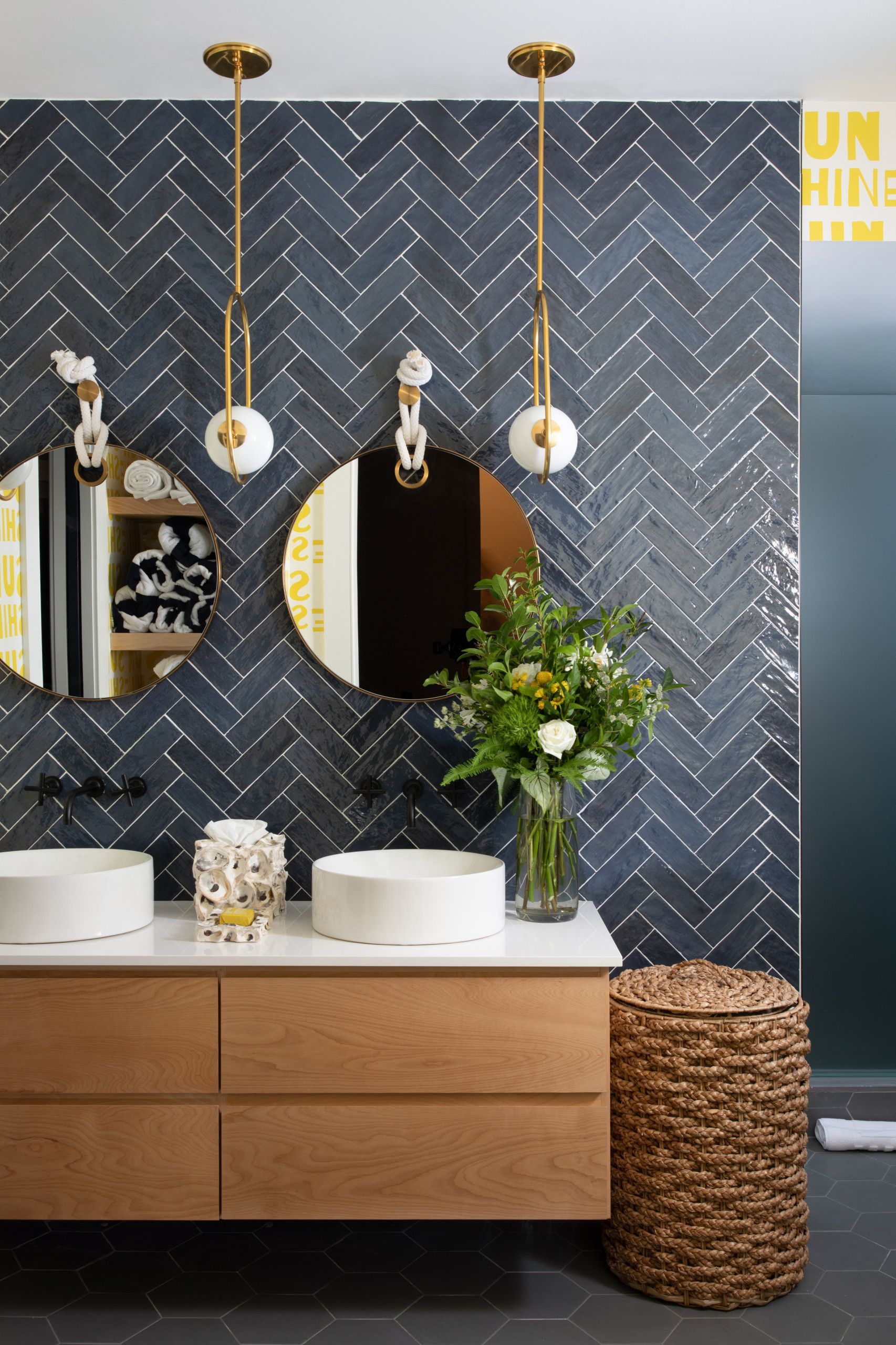 Modern bathroom vanity with two round mirrors, wooden cabinet, and dark herringbone tile wall