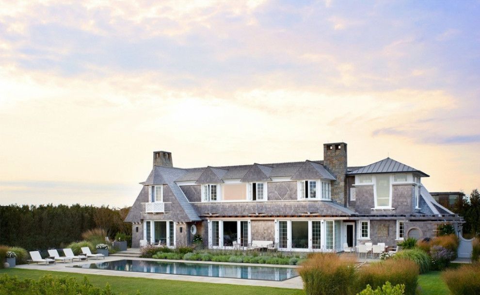 Large stone house with a gray roof and pool in a landscaped yard at sunset