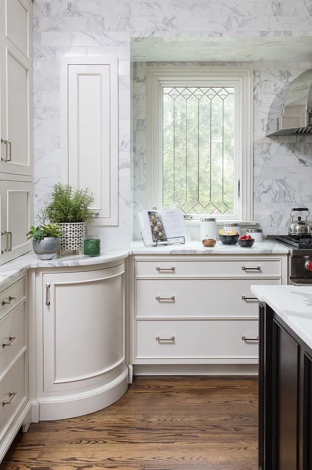 Bright white kitchen with marble walls, wood floor, and a window over the countertop.
