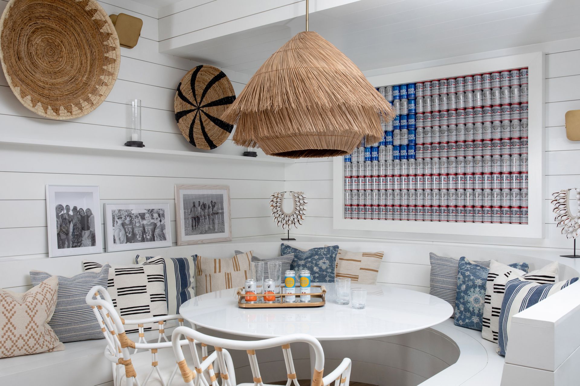 Cozy white coastal dining nook with round table, woven pendant lights, and patterned cushions under framed art