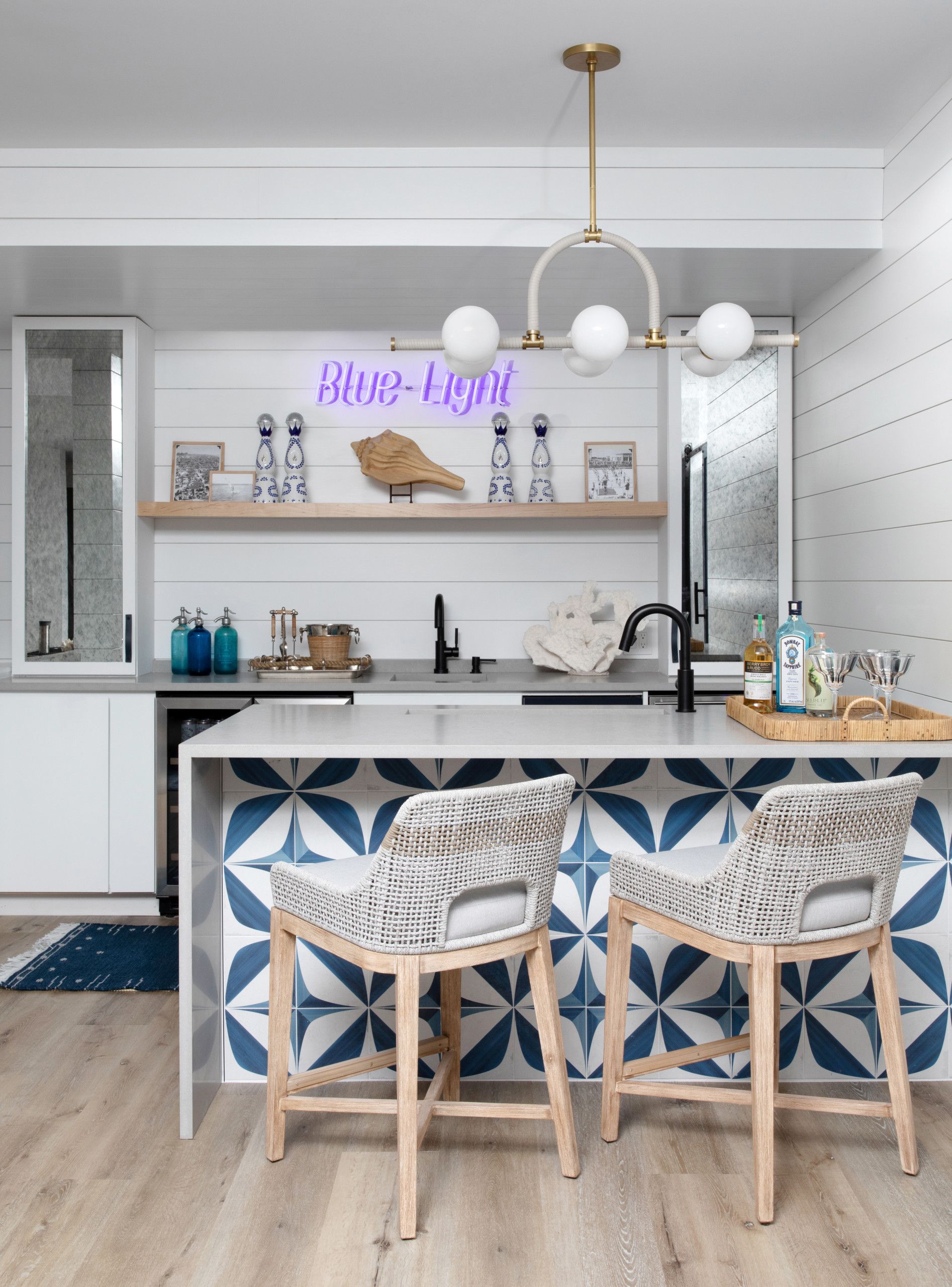 Bright modern kitchen with island, blue geometric backsplash, and two wooden chairs with patterned cushions
