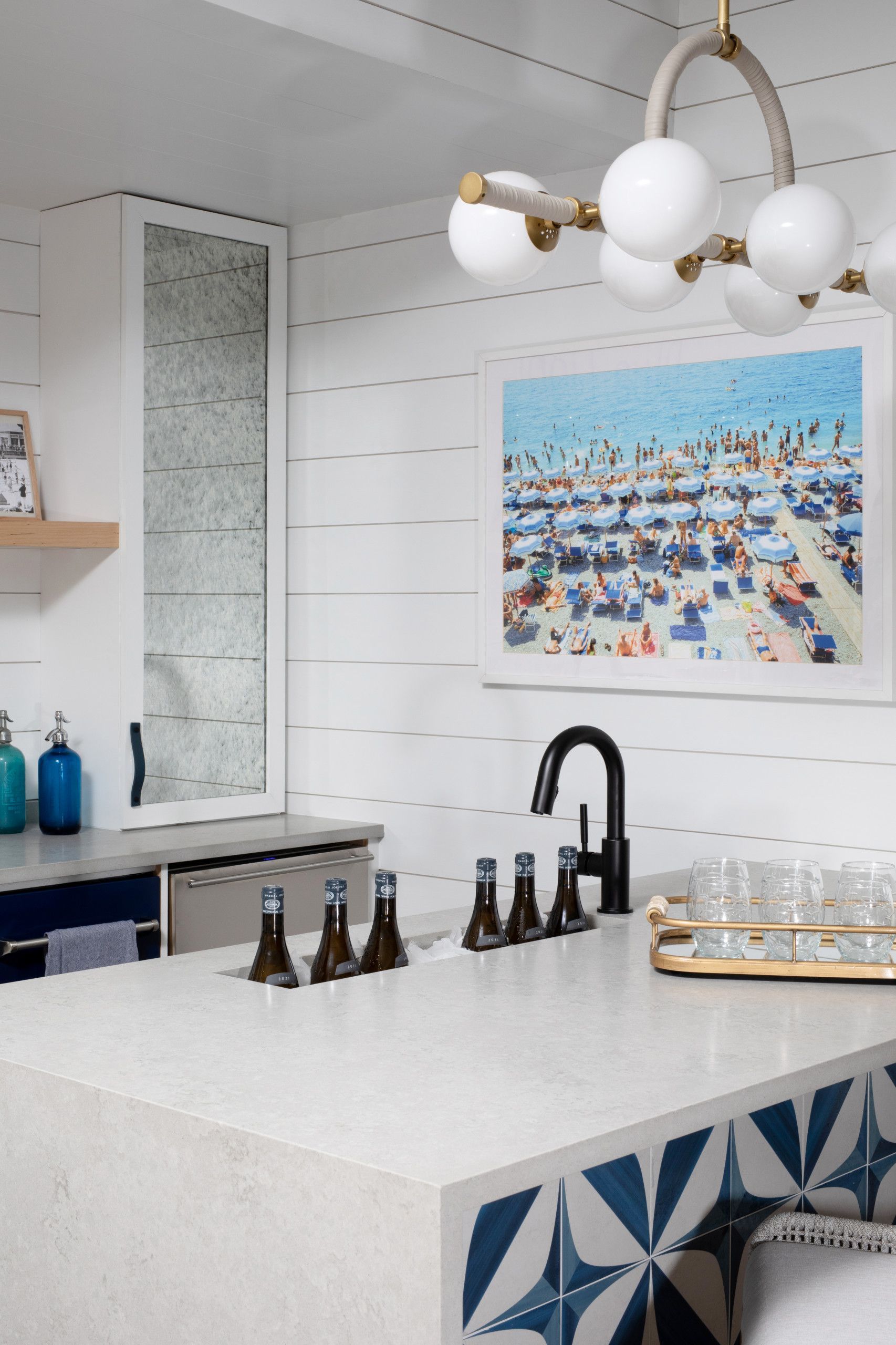 Modern kitchen with white tile backsplash, black faucet, white island, pendant light, and beach artwork