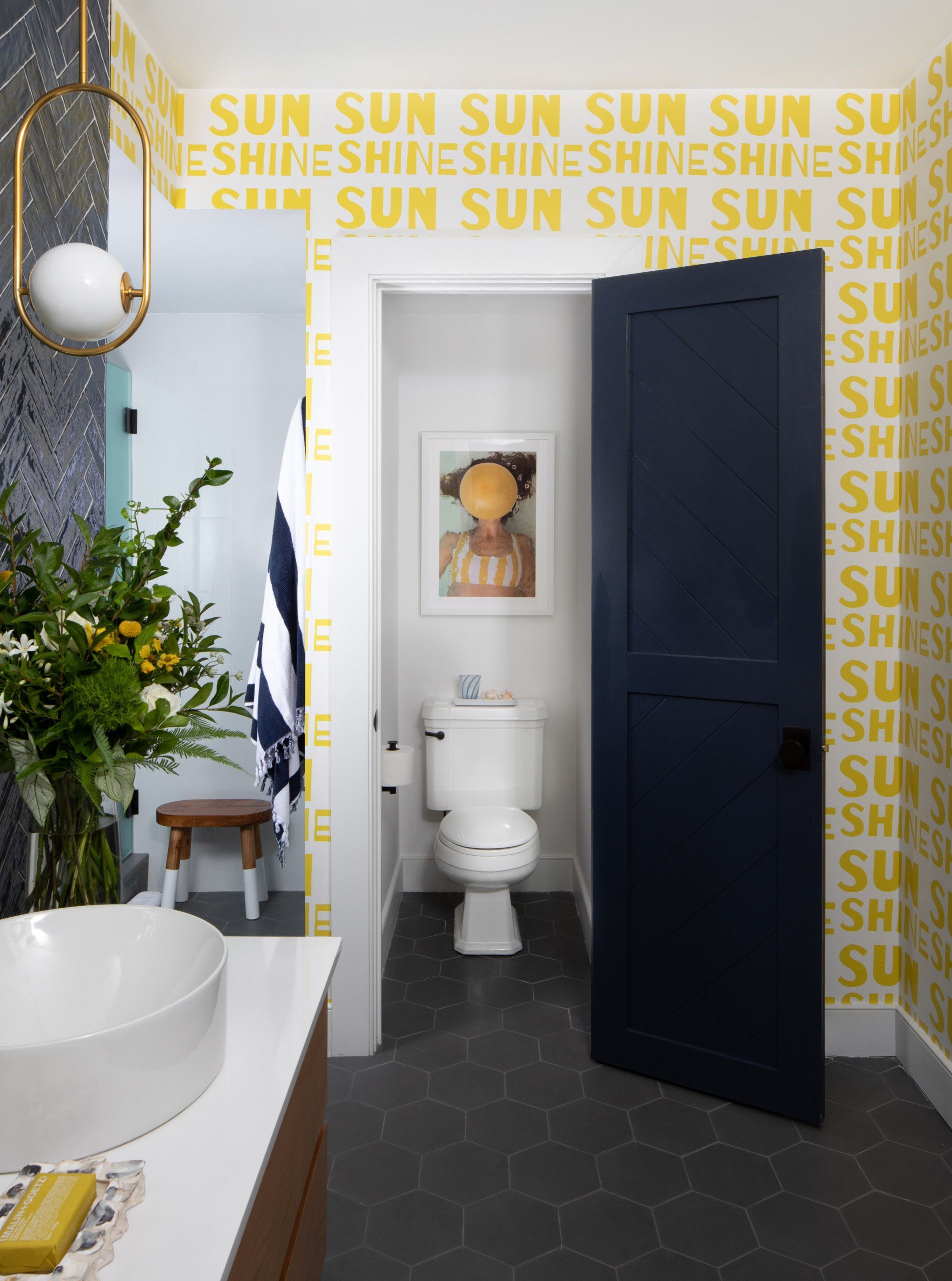 Small bathroom with bold yellow wallpaper, dark blue door, and white sink in the foreground