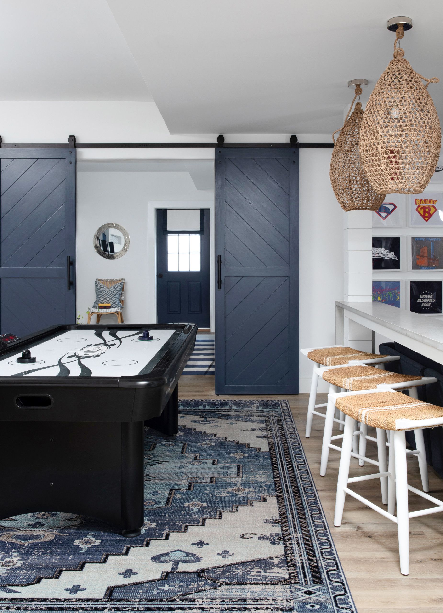 Modern game room with a pool table, blue sliding doors, patterned rug, and woven pendant lights