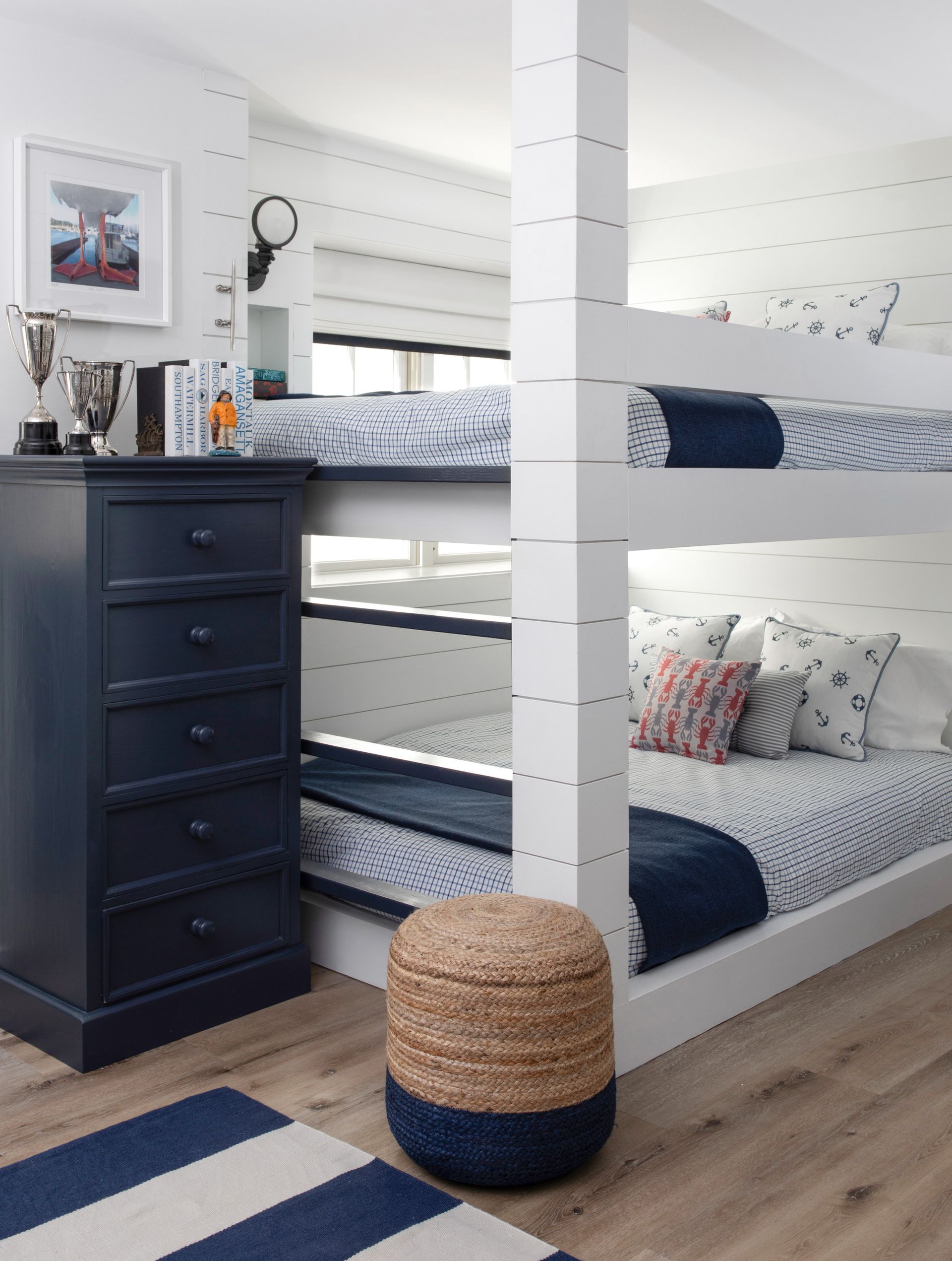 Loft bed nook with navy drawers, woven stools, and blue-and-white bedding in a bright room