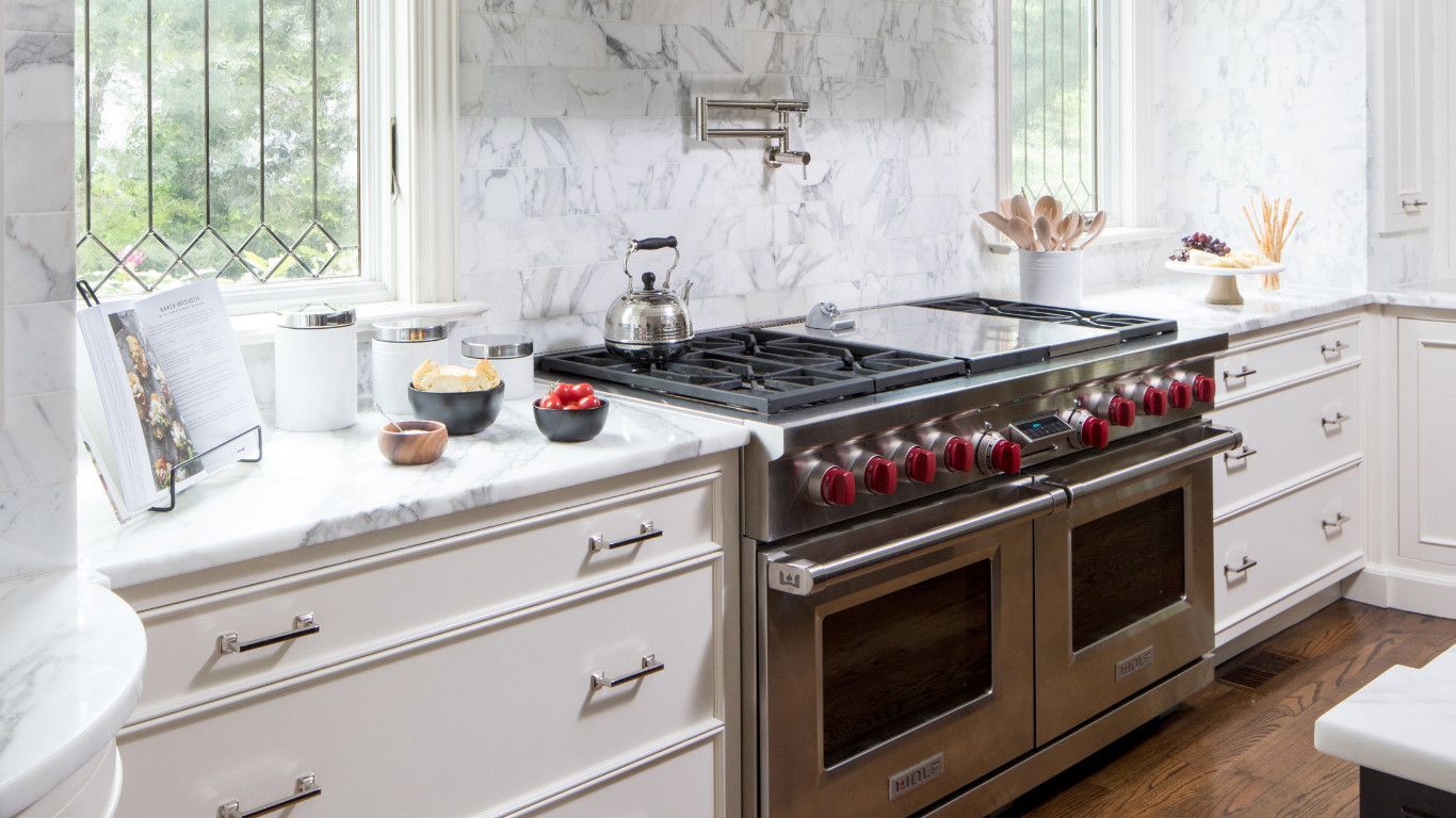 Bright white kitchen with a stainless gas range, marble backsplash, and window seat by the sink.