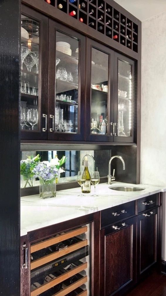 Dark wood wet bar with glass-front cabinets, wine rack, white countertop, sink, and flowers