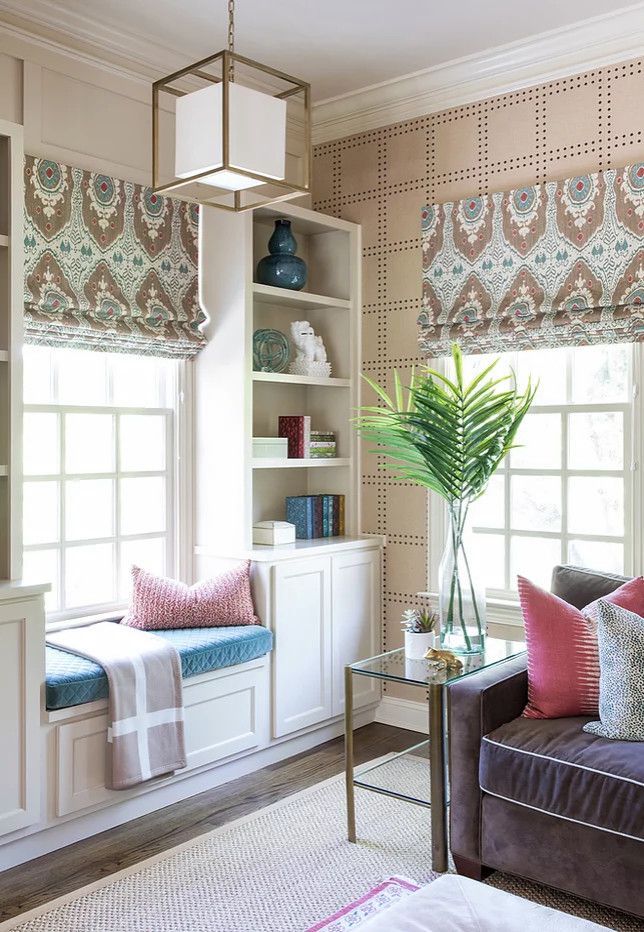 Bright living room nook with built-in shelves, patterned shades, window seat, and a sofa with pink pillows