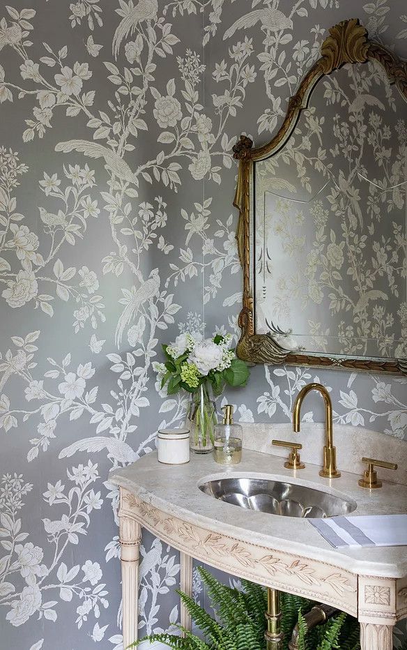 Elegant bathroom vanity with patterned wallpaper, ornate mirror, gold faucet, and flowers in a glass vase