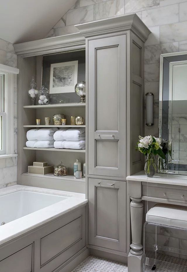 Elegant gray bathroom with built-in shelving, bathtub, vanity, and mirror on tiled walls