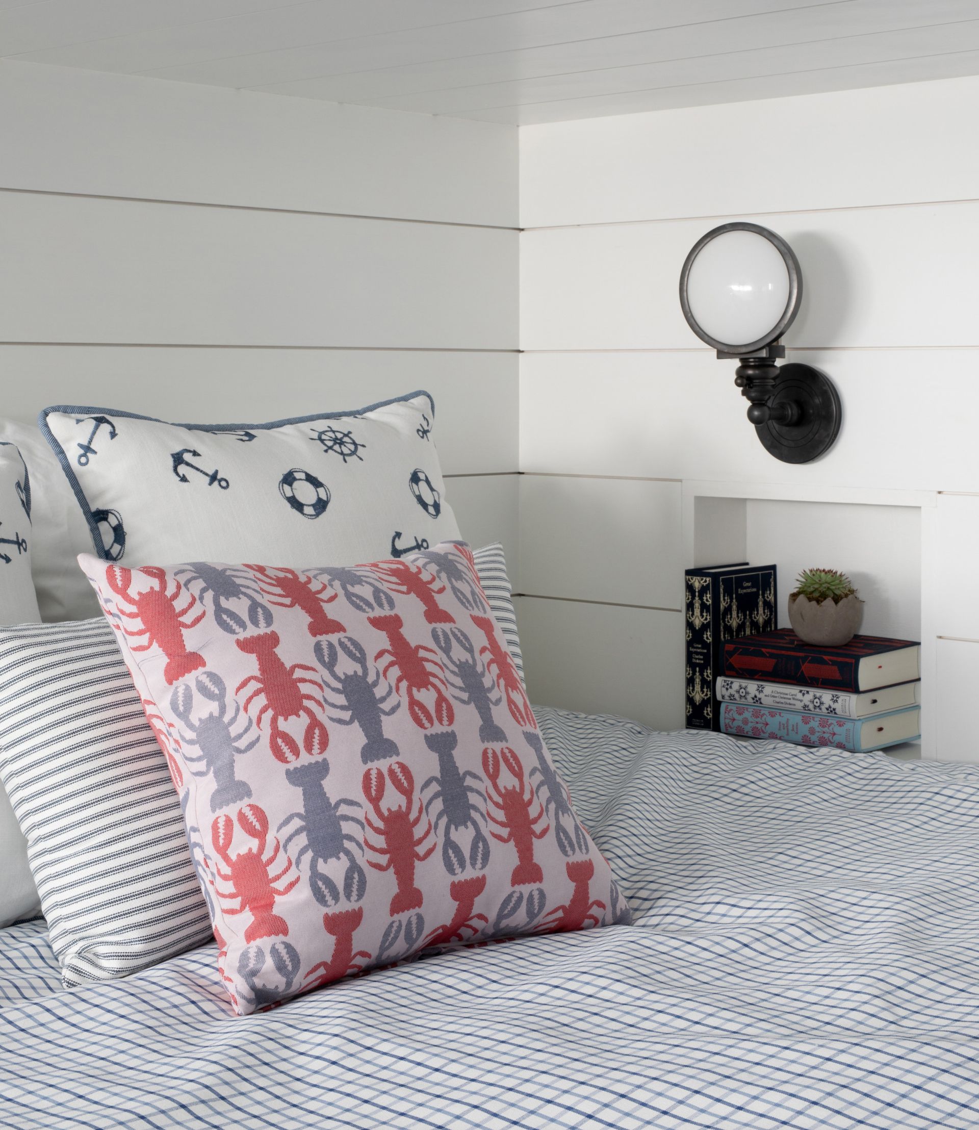 Cozy bed with patterned pillows and white shiplap wall, plus small shelf and round mirror