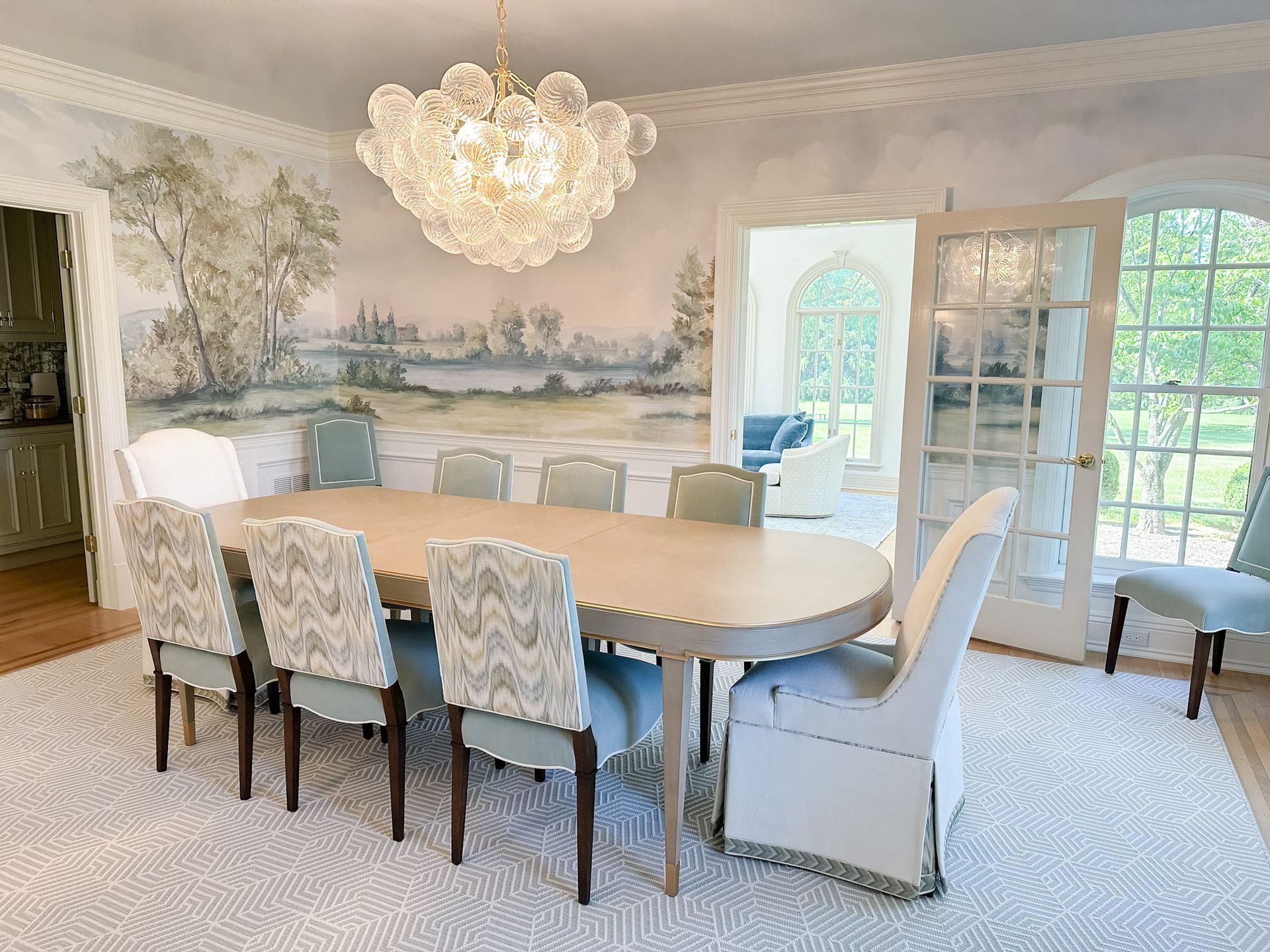 Elegant dining room with floral chairs, chandelier, large oval table, and mural wall art