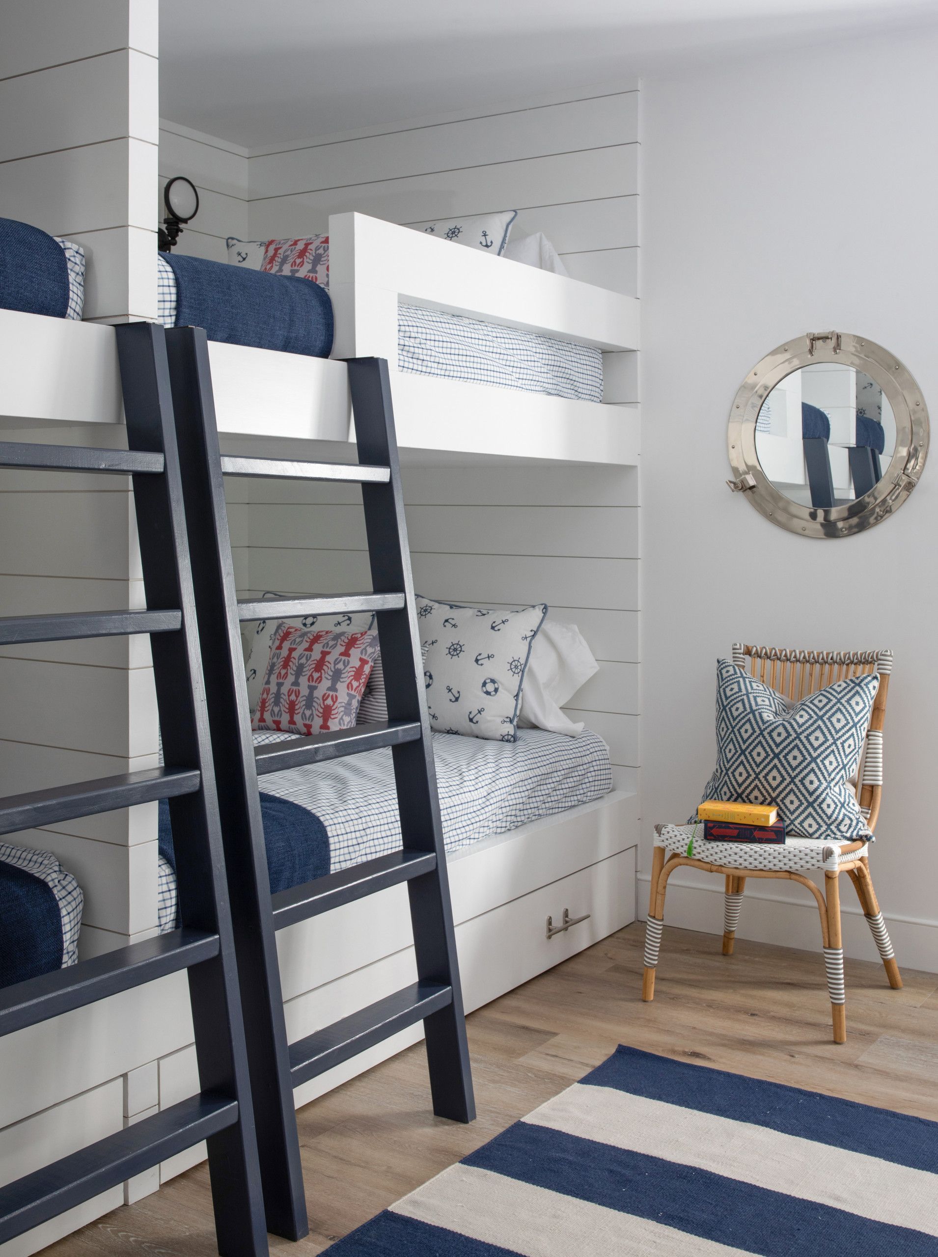 Navy bunk bed in a white child’s room with striped rug, chair, and round mirror on the wall