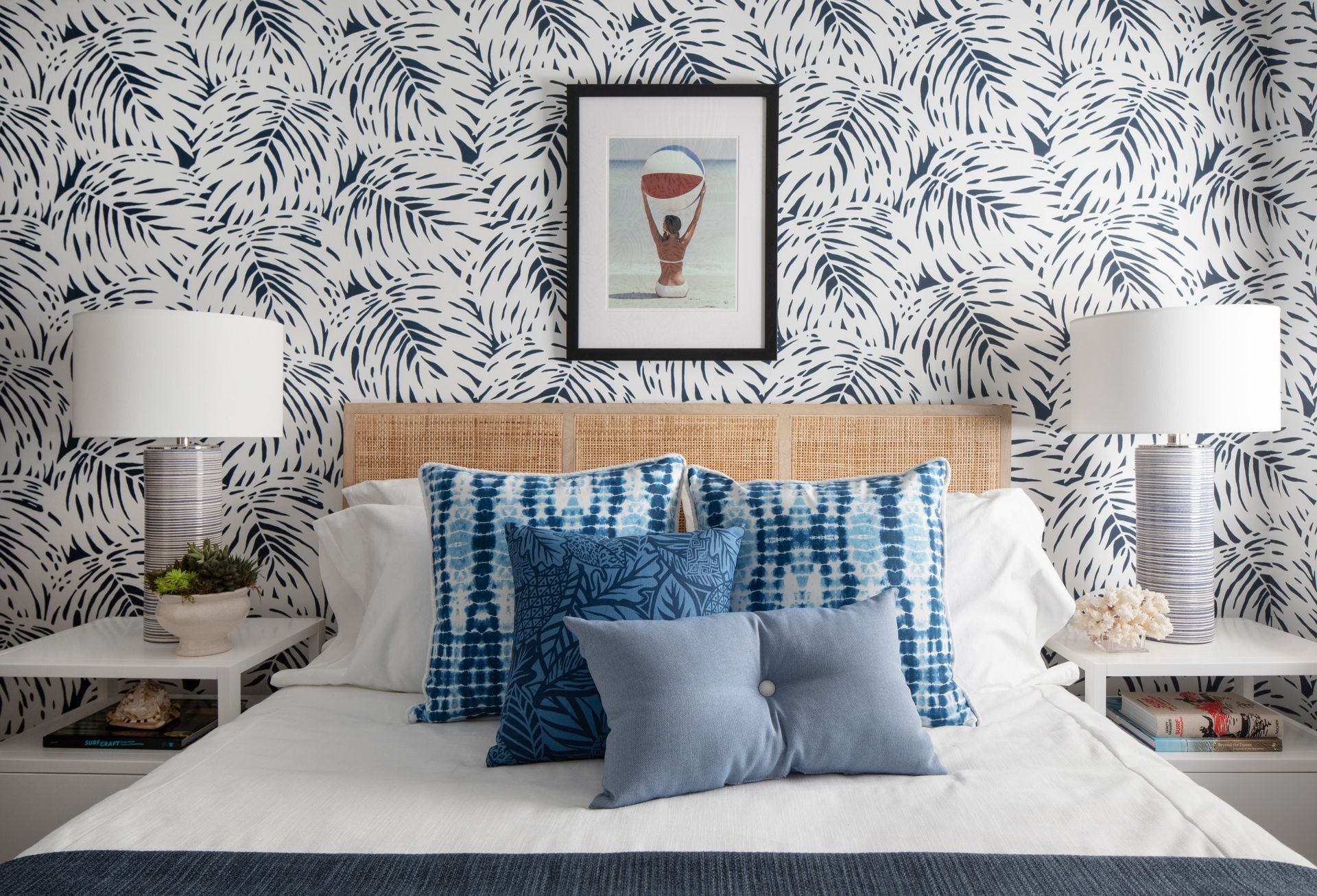 Blue-and-white patterned bedroom with a wicker headboard, layered pillows, and matching lamps