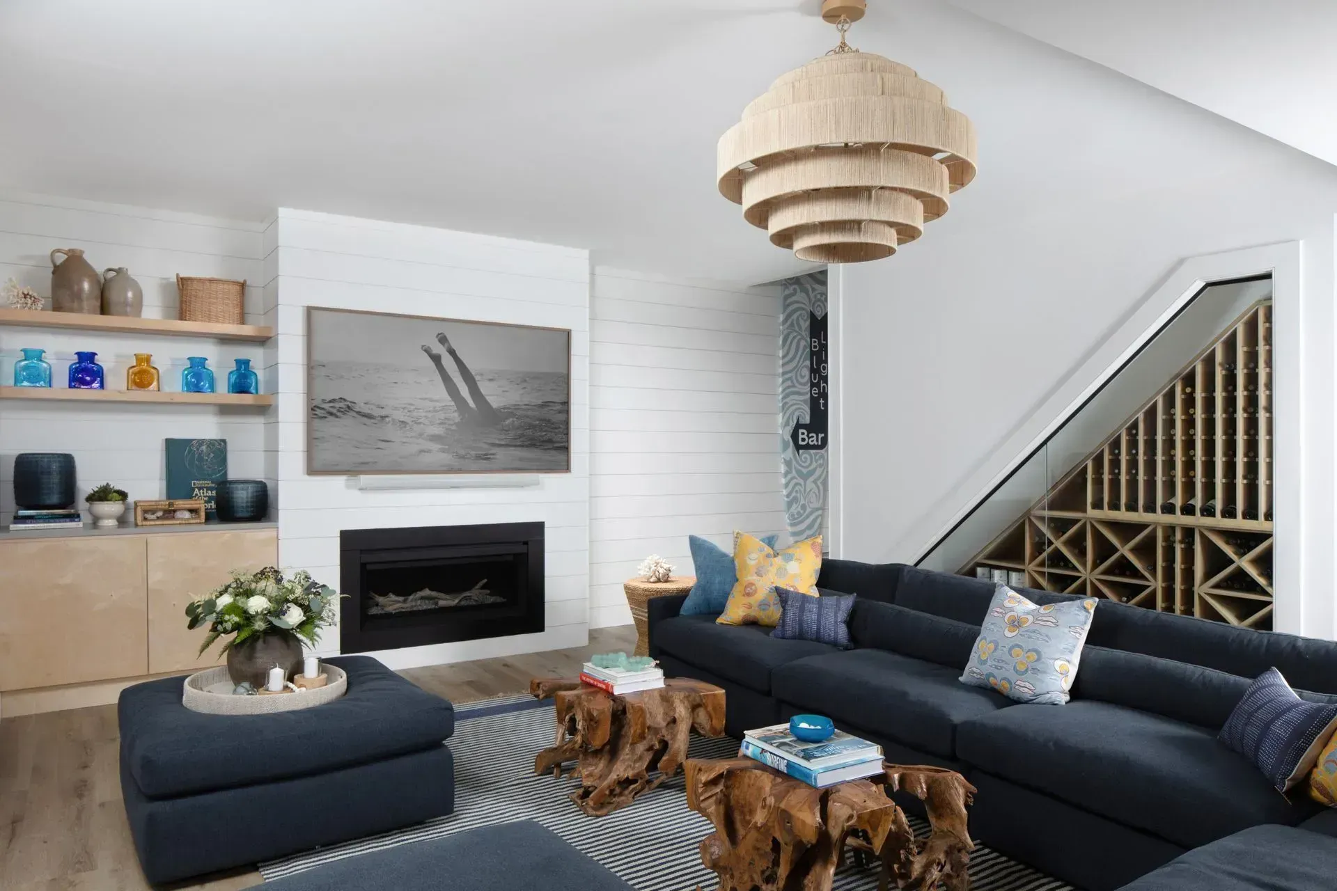 Modern living room with navy sectional, fireplace, wood coffee table, and staircase wine storage
